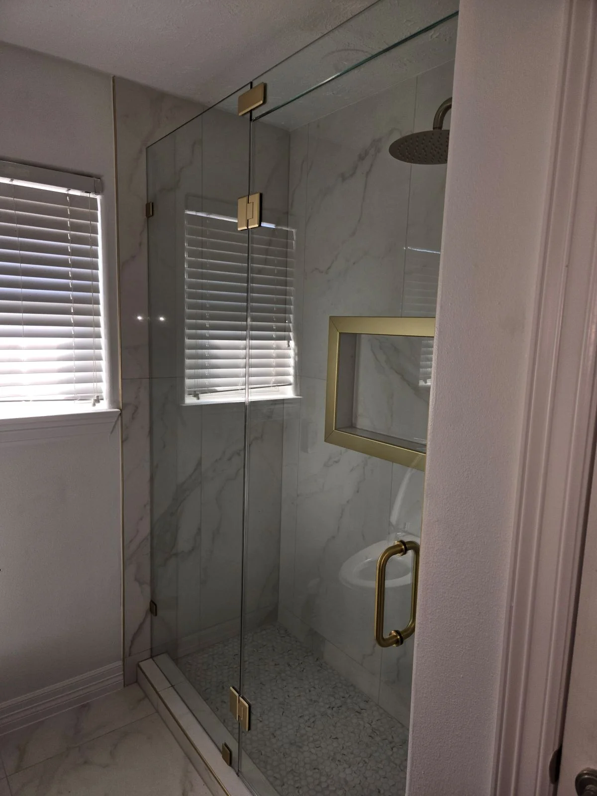 Frameless glass shower with marble walls, brass fixtures, and rainfall showerhead