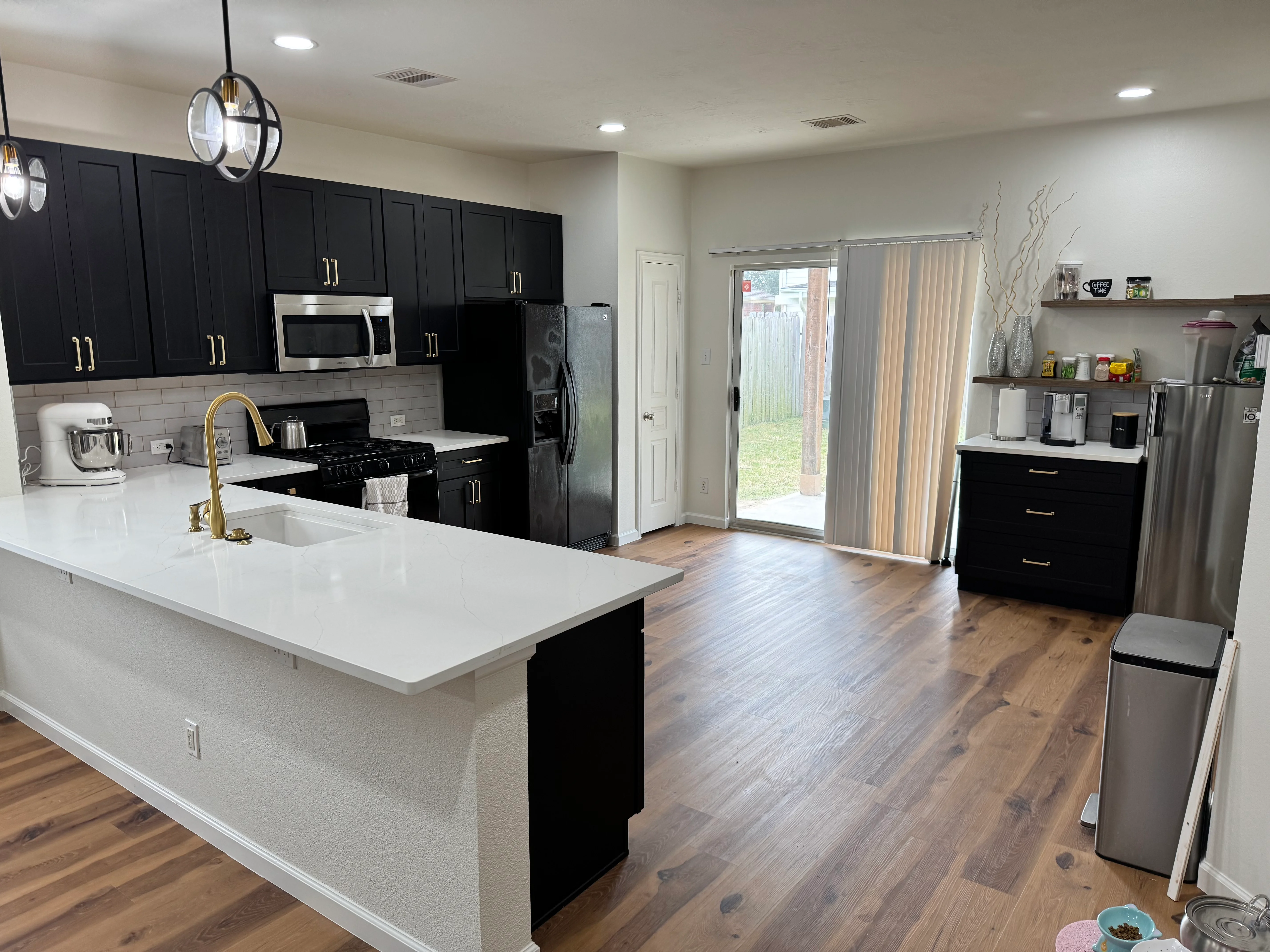Modern kitchen with black cabinets, white quartz counters, and island opening to backyard