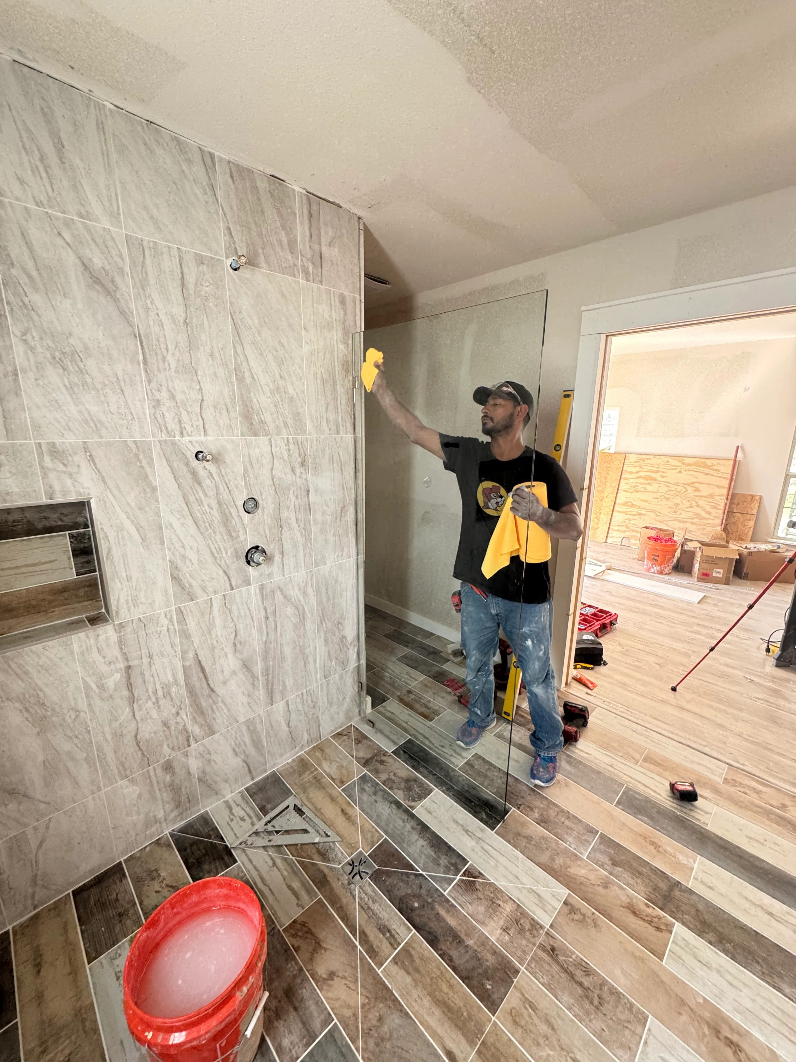 Contractor installing large-format tile in newly remodeled shower with frameless glass enclosure