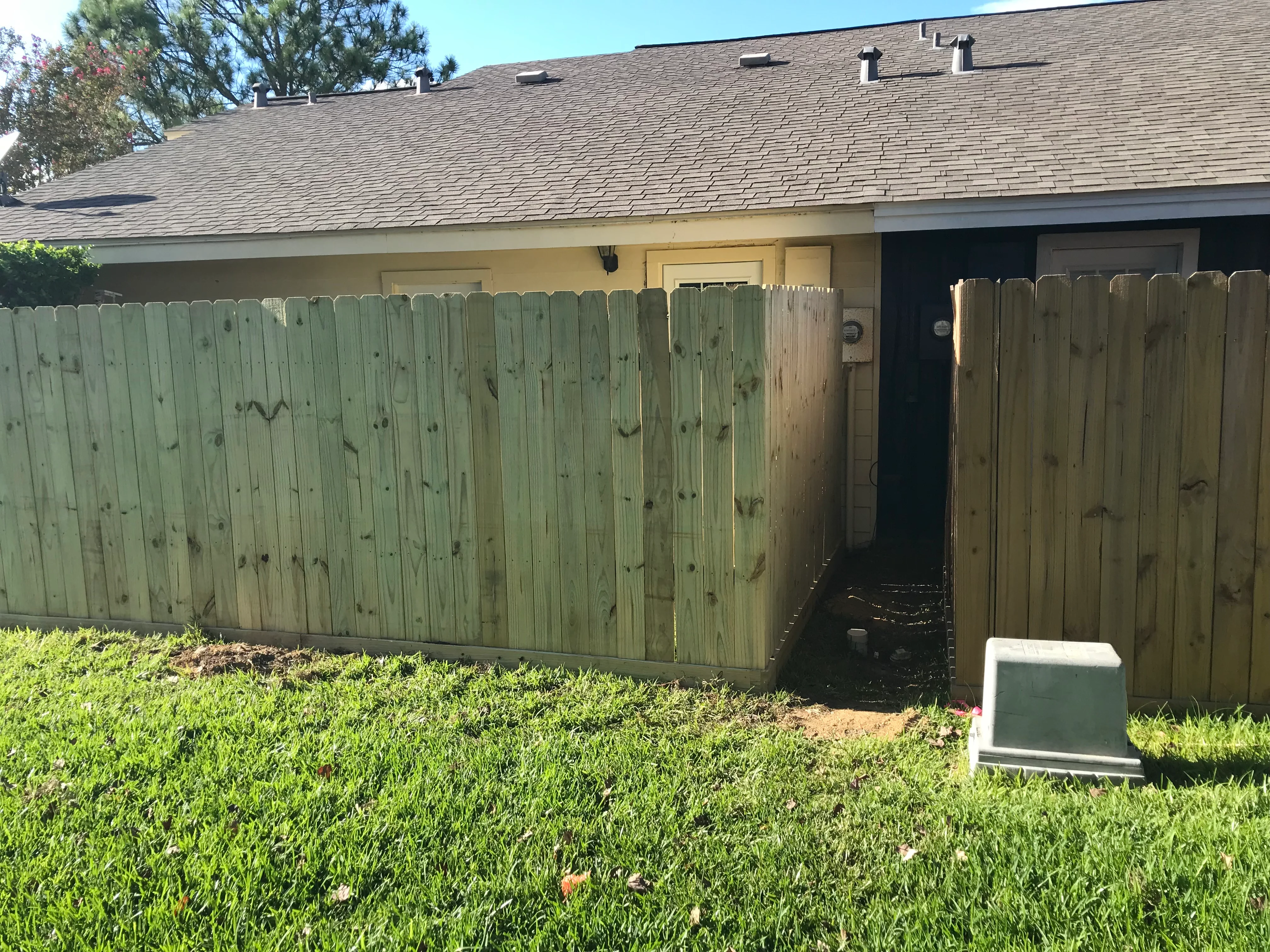 Newly installed pressure-treated wood privacy fence with gate opening along residential backyard