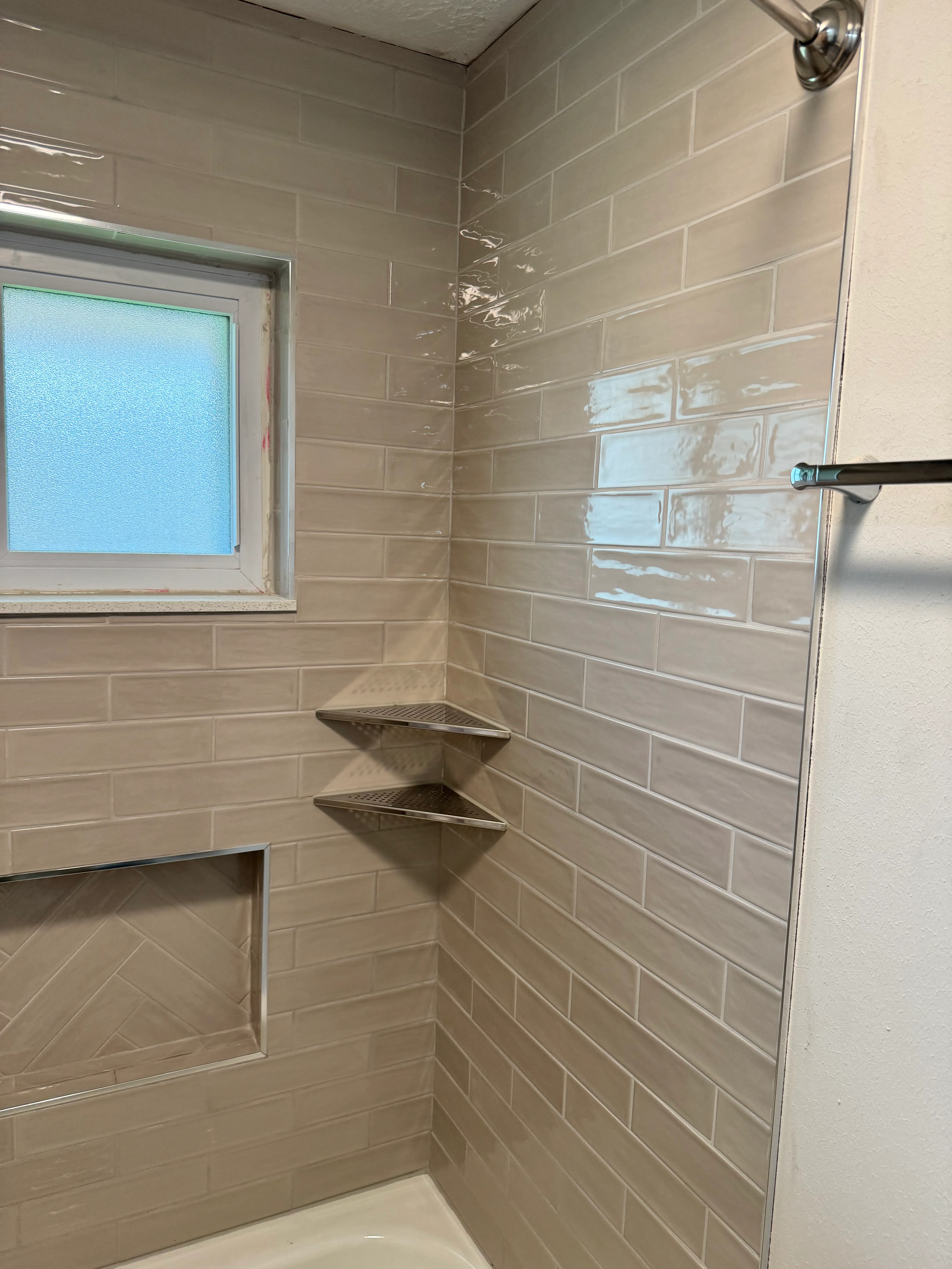 Newly tiled shower enclosure with beige subway tiles, corner shelves, and frosted window