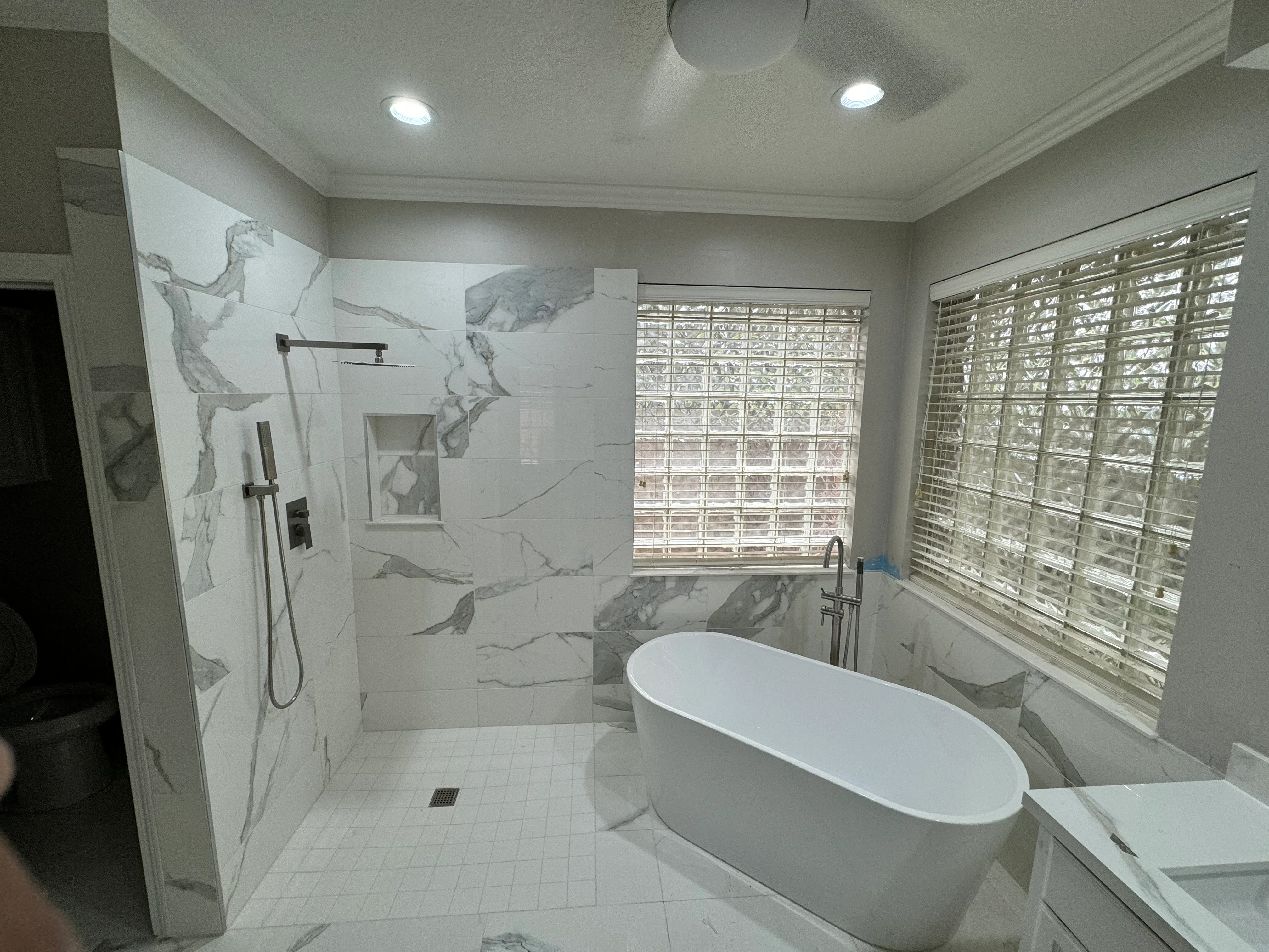 Modern bathroom with marble shower enclosure, white freestanding tub, and recessed lighting