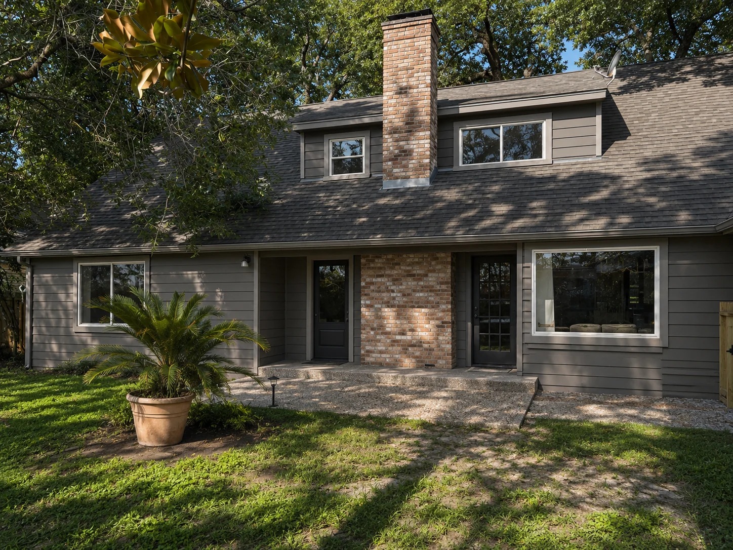 Modern two-story home with gray siding, brick chimney, and new windows