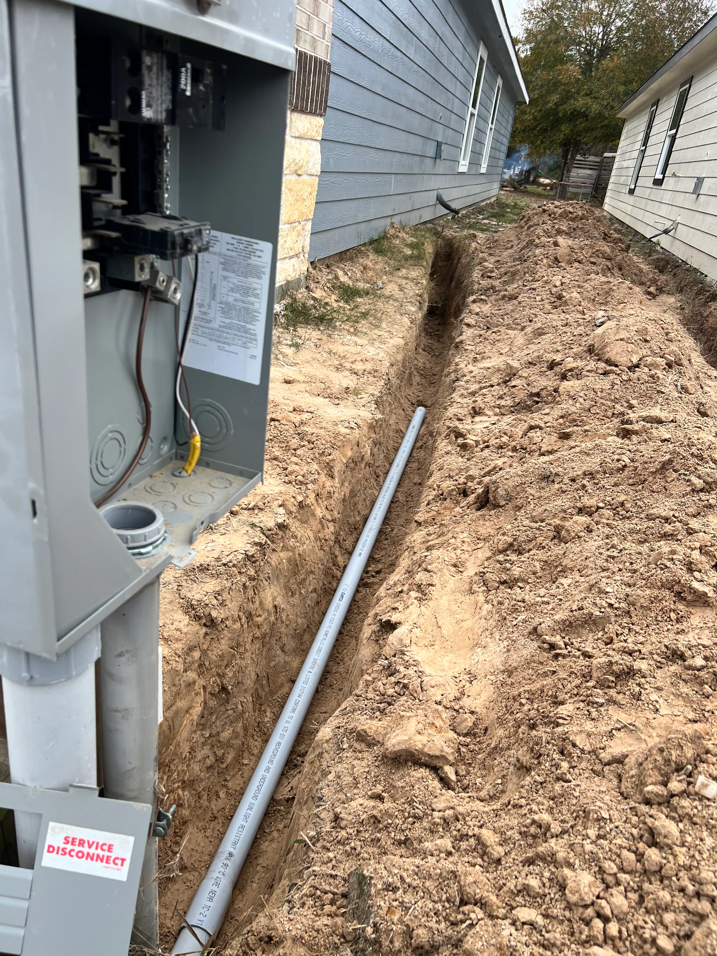 Underground PVC utility line installation in excavated trench beside residential home