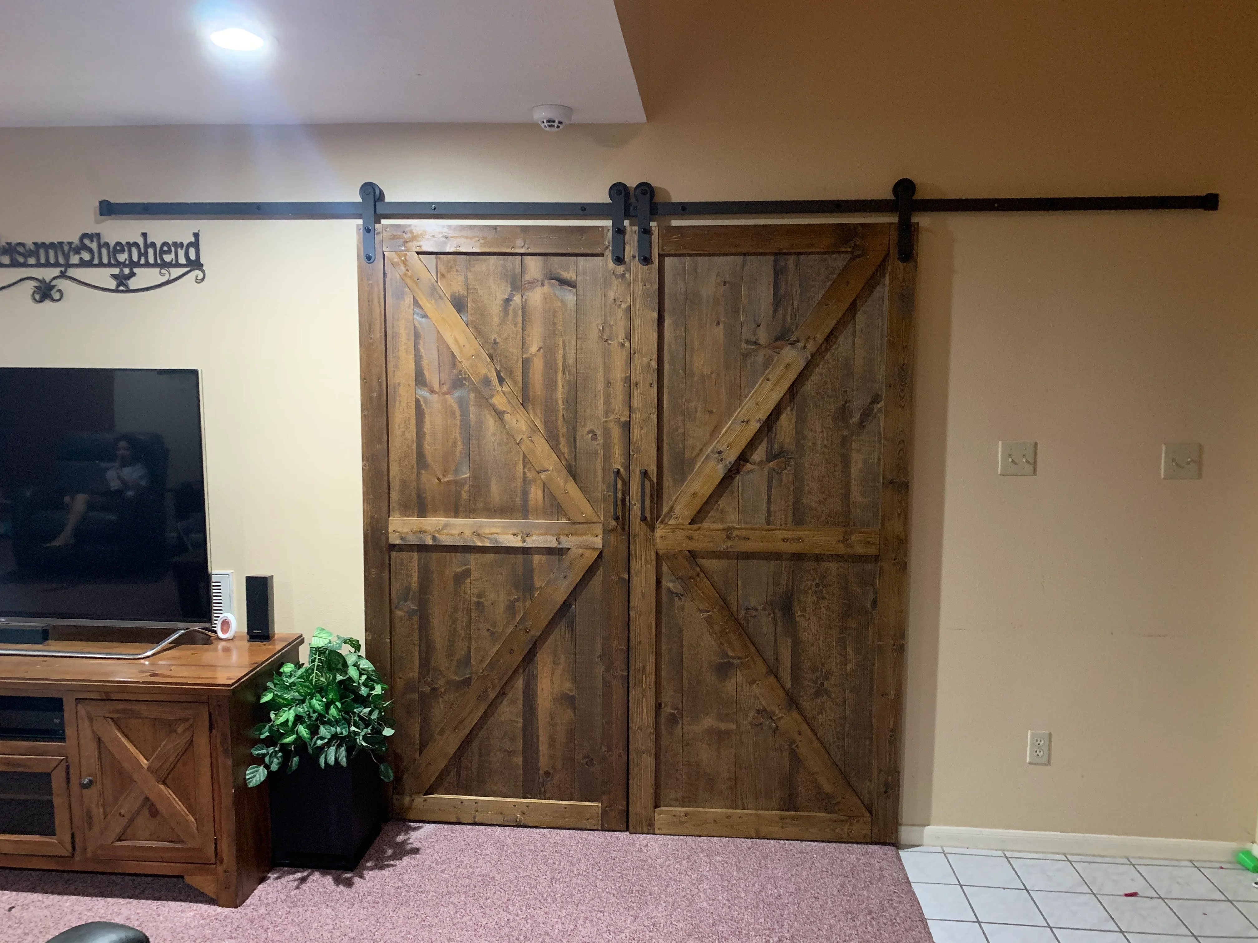 Two rustic wooden barn doors with X-bracing on black sliding track hardware in home interior