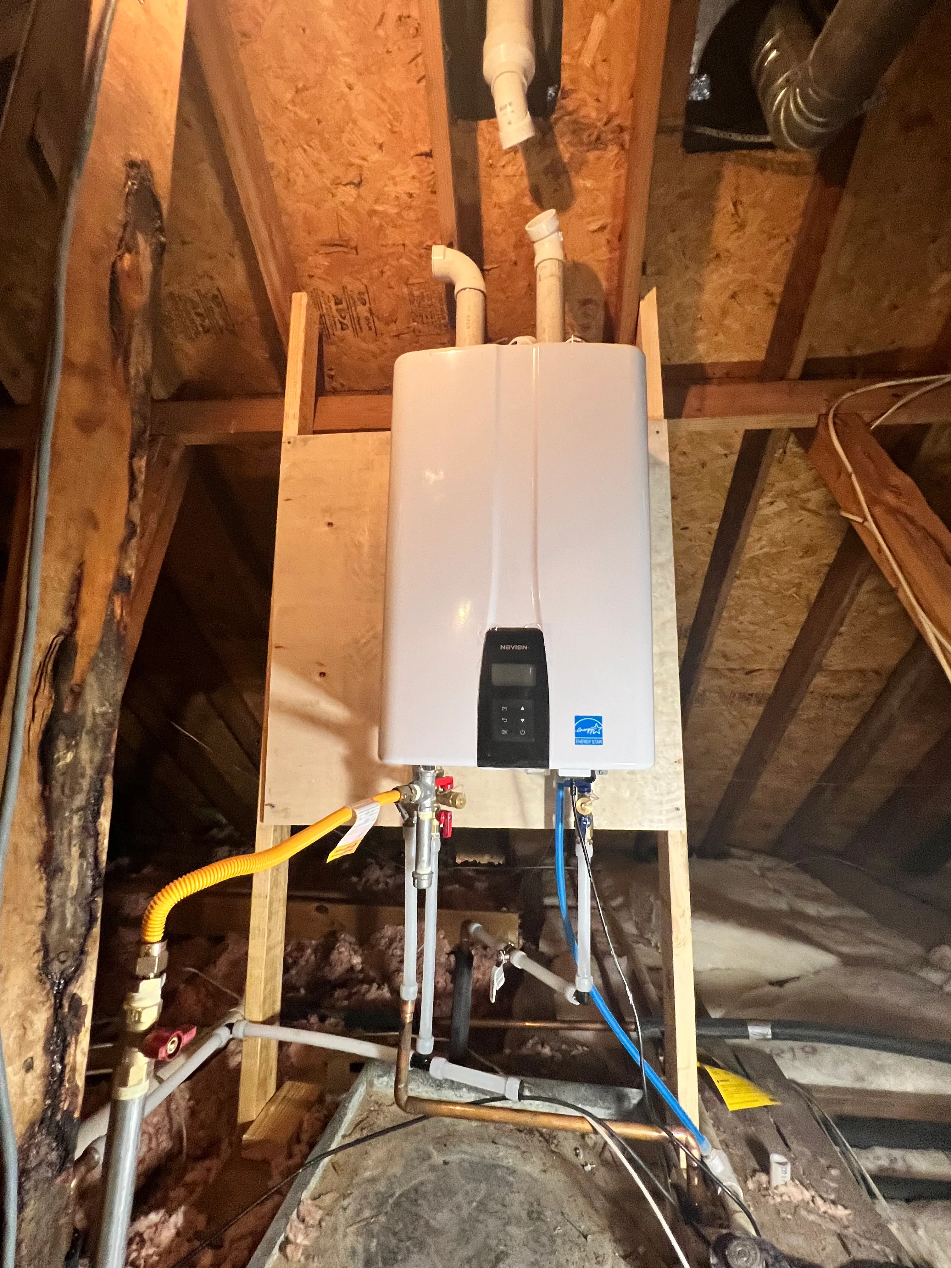 White tankless water heater mounted in attic with gas and water line connections