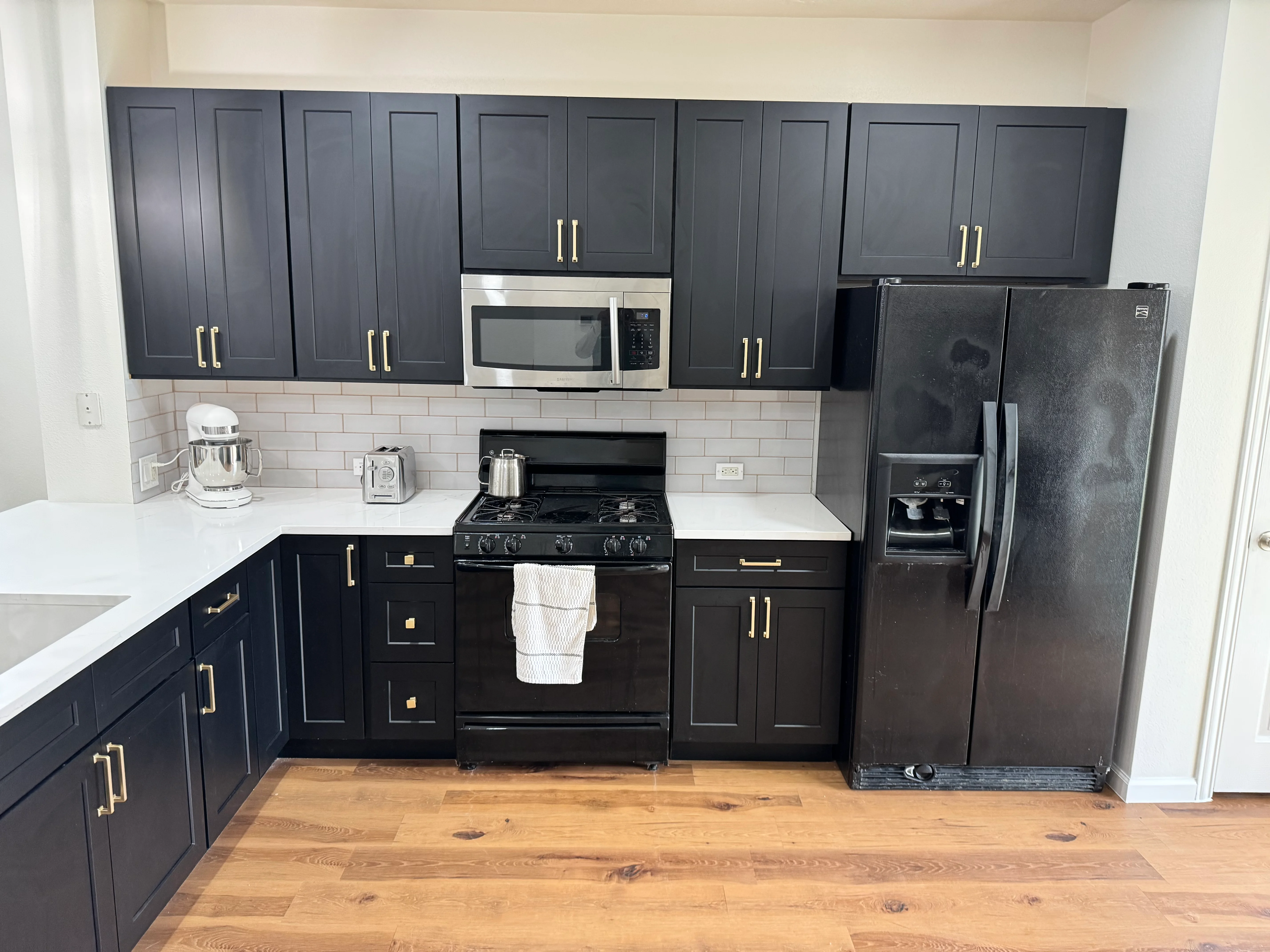 Modern kitchen with dark blue cabinets, white countertops, stainless steel appliances, and hardwood floors