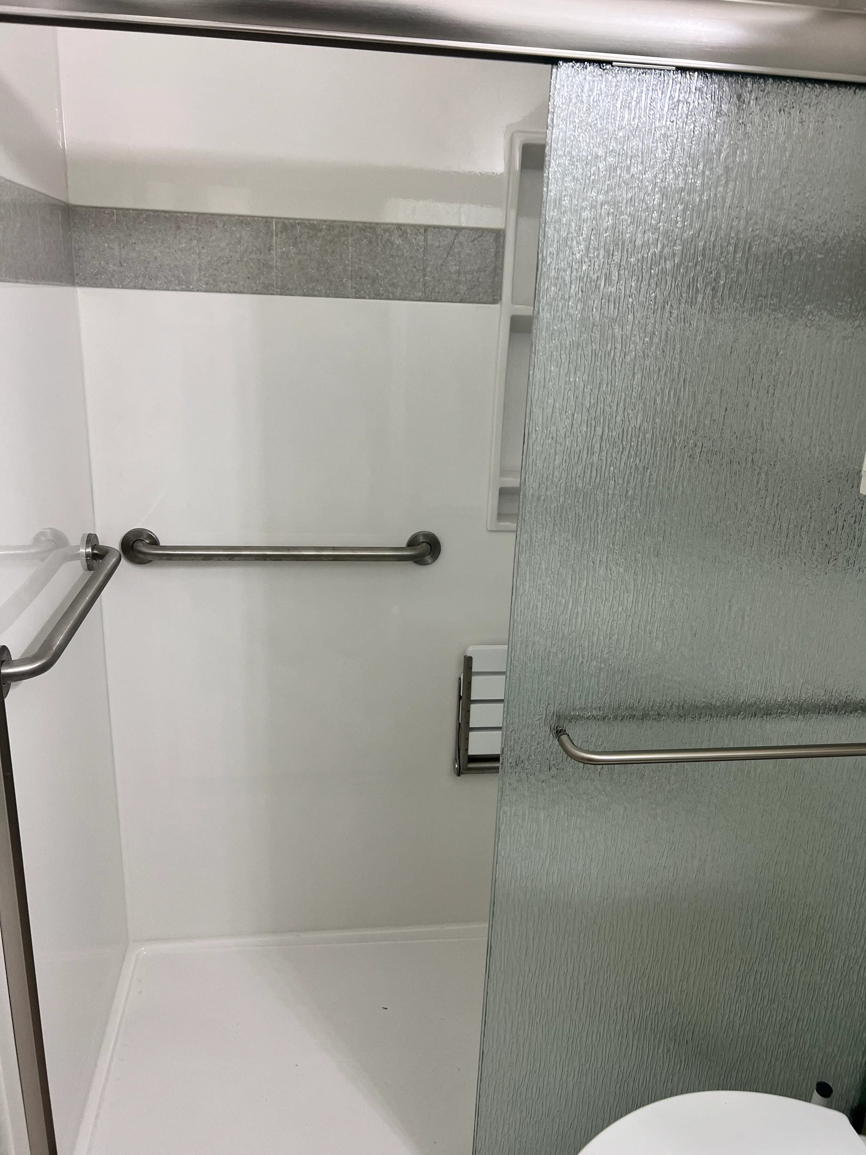 Modern shower enclosure with gray textured tile walls, white accent stripe, and black grab bars