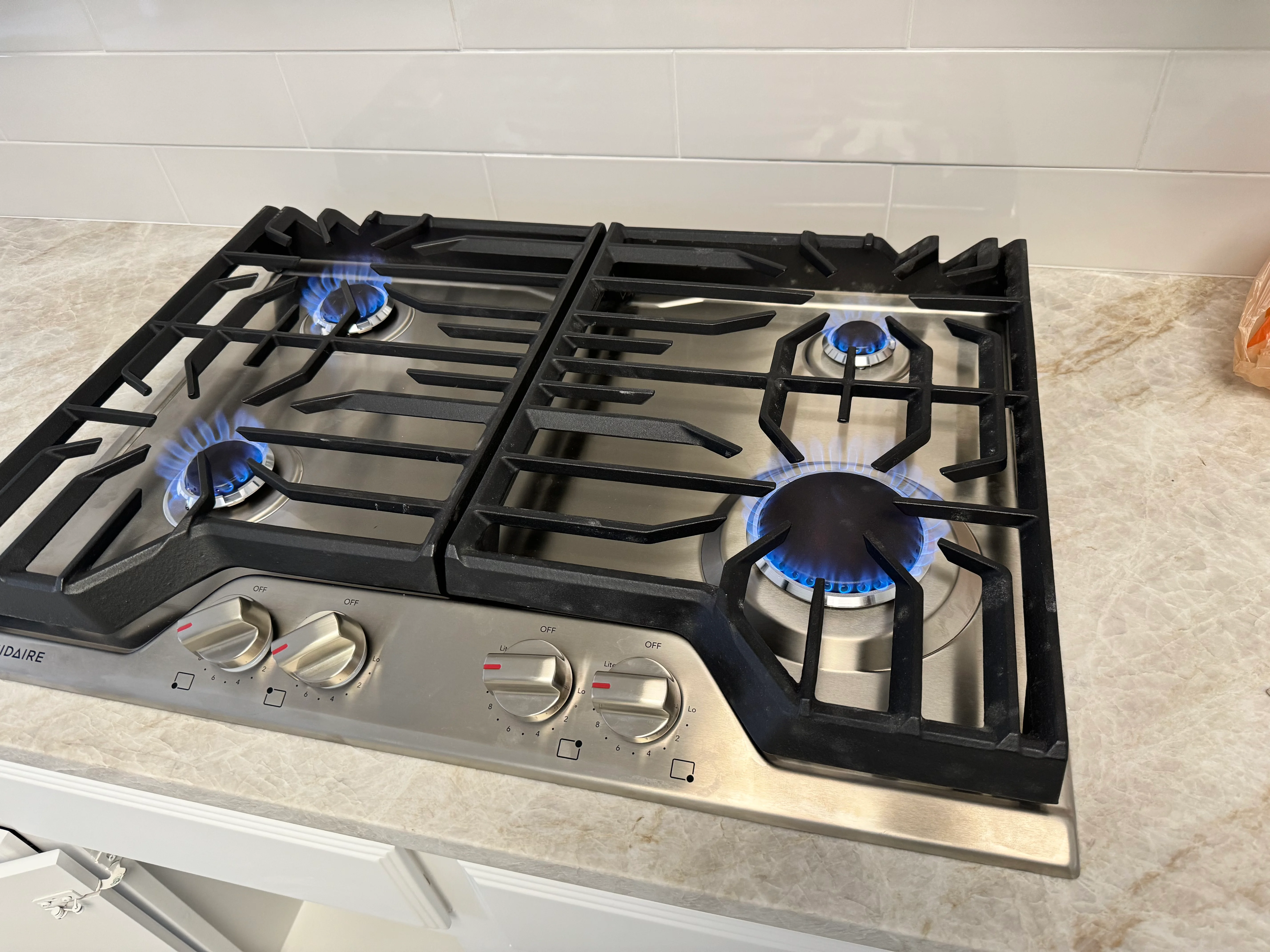 Four-burner stainless steel gas cooktop with blue flame burners lit on quartz countertop