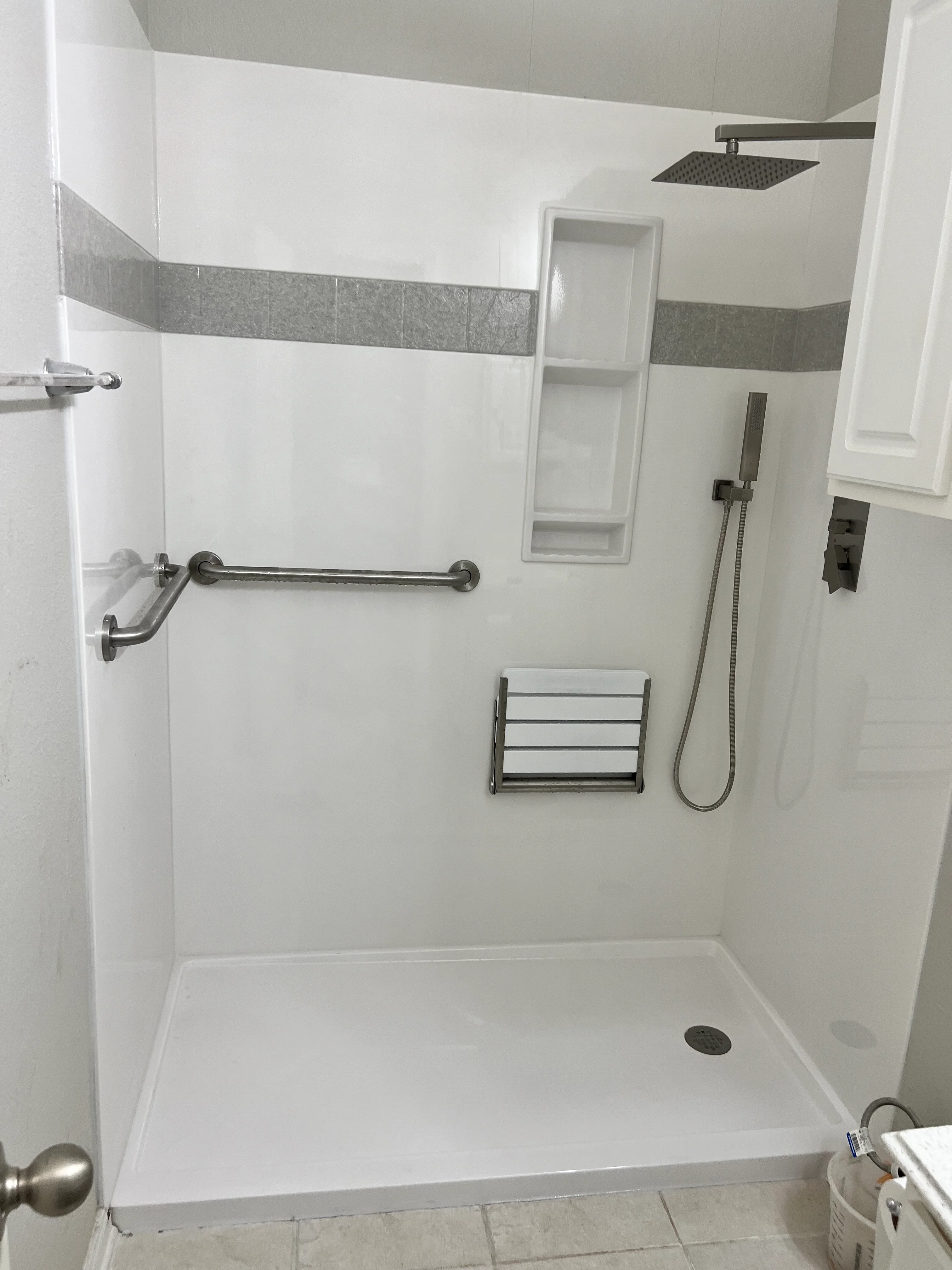 Modern walk-in shower with white walls, gray tile accent band, and brushed nickel fixtures