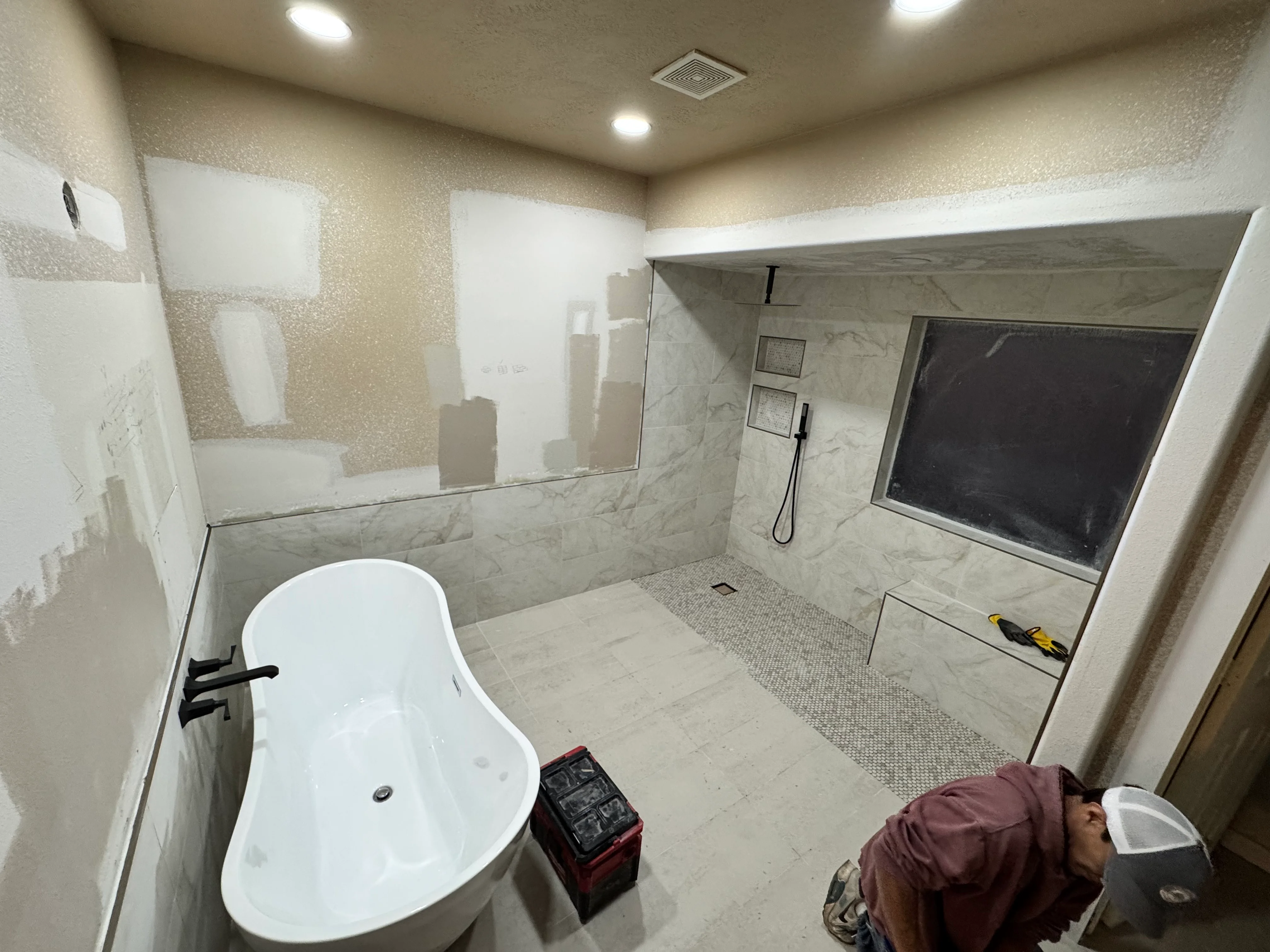 Modern master bathroom with white freestanding tub, marble tile, and glass shower enclosure