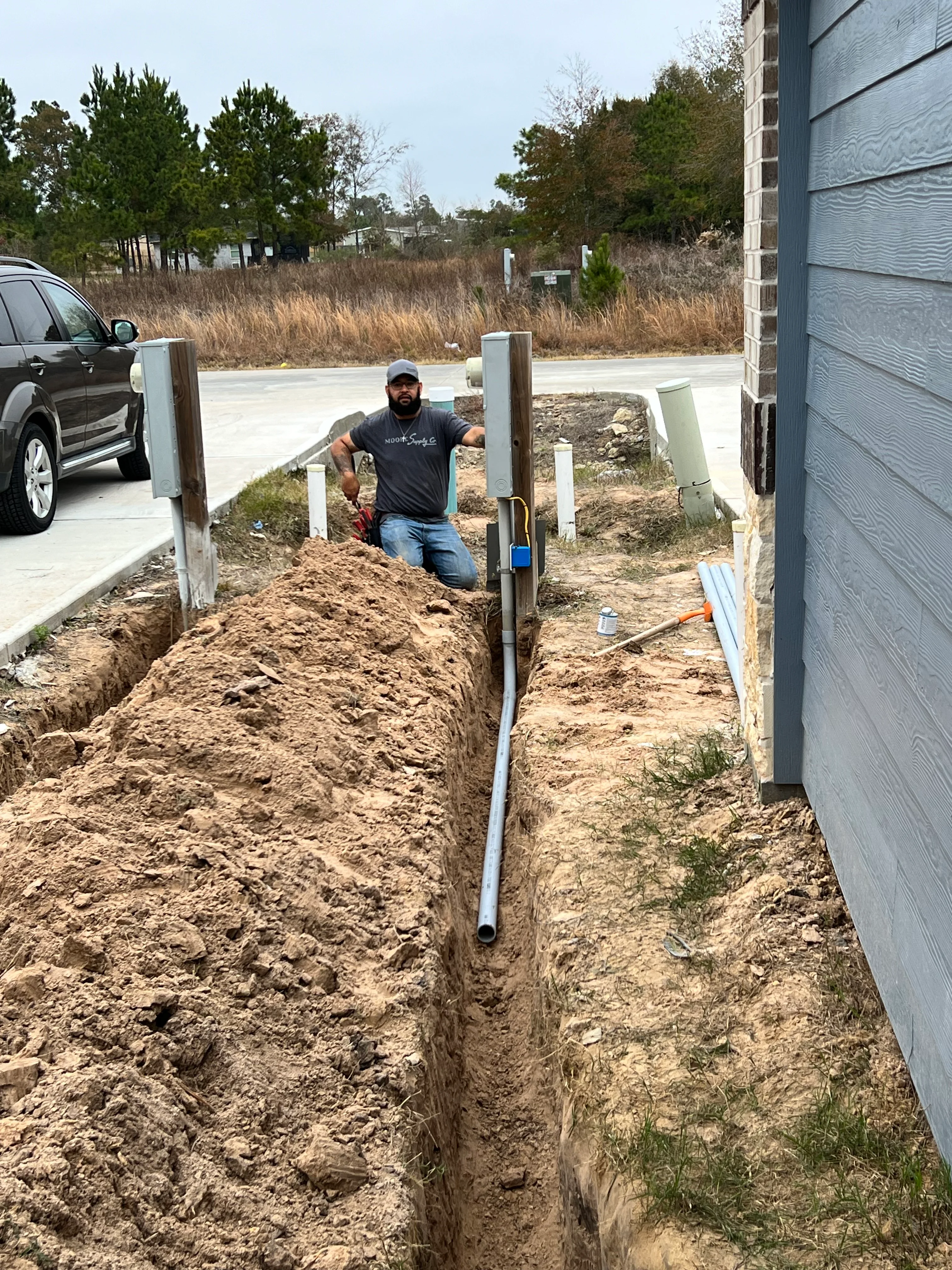 Worker installing underground drainage pipe in excavated trench beside residential foundation