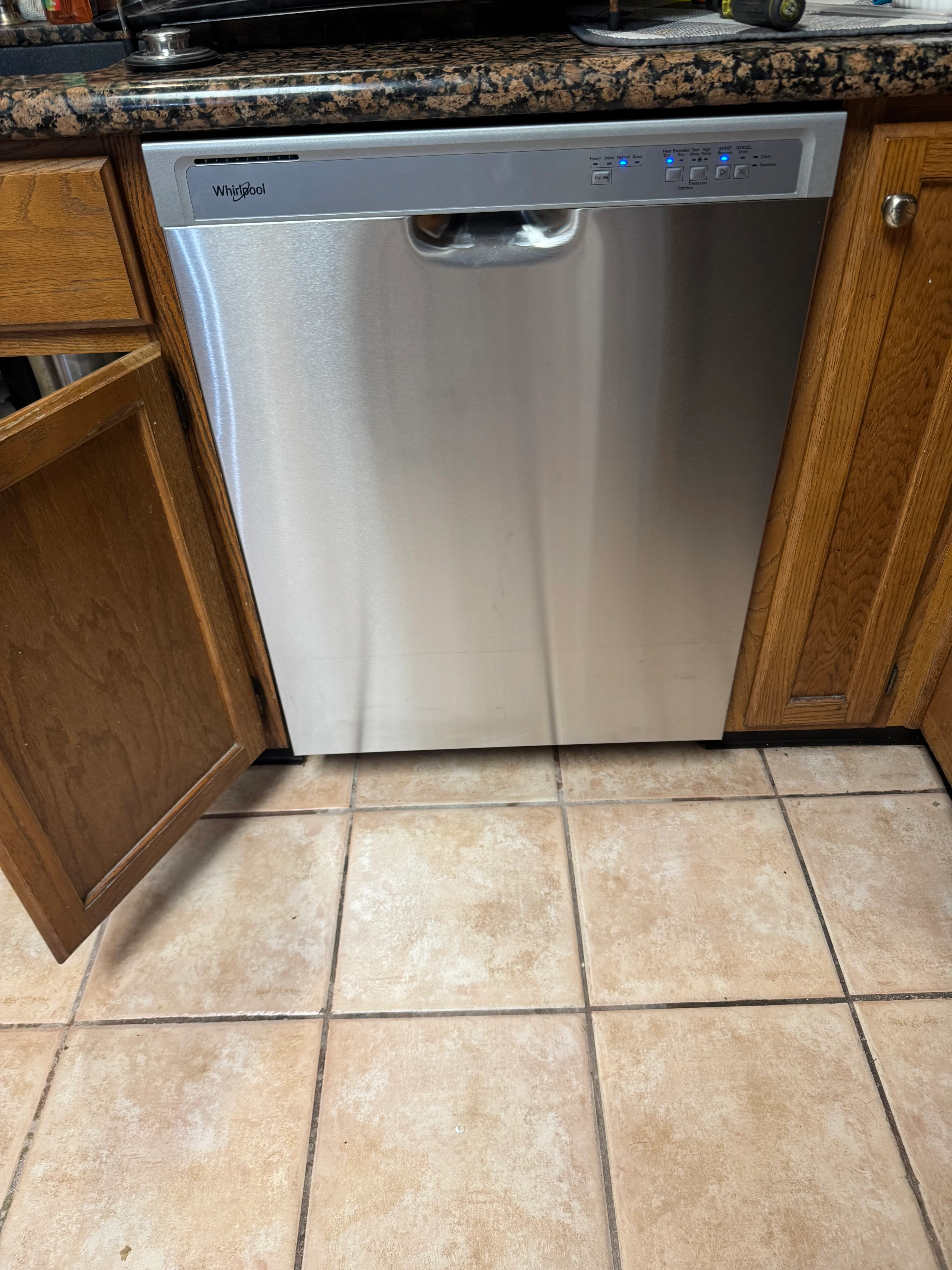 Stainless steel Whirlpool dishwasher installed between oak cabinets with granite countertop