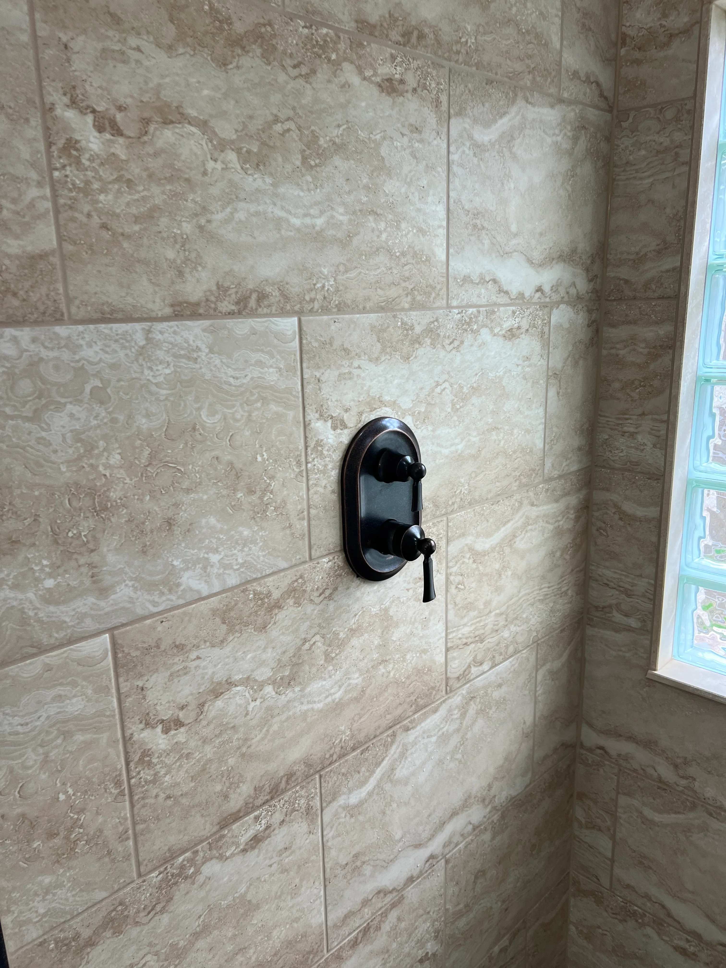 Travertine tile shower wall with black valve fixture and lever handle