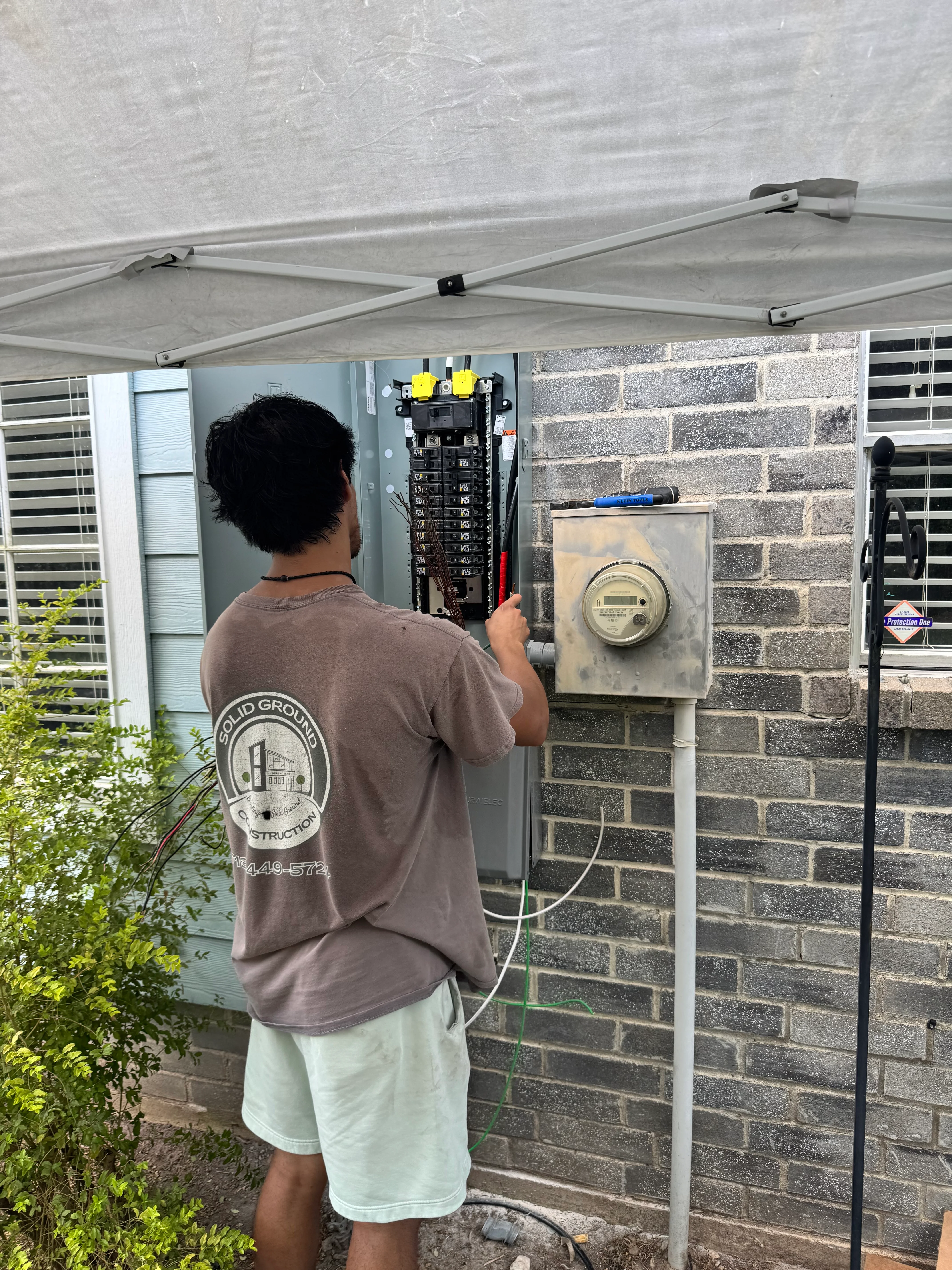 Electrician installing main electrical panel and meter box on brick home exterior