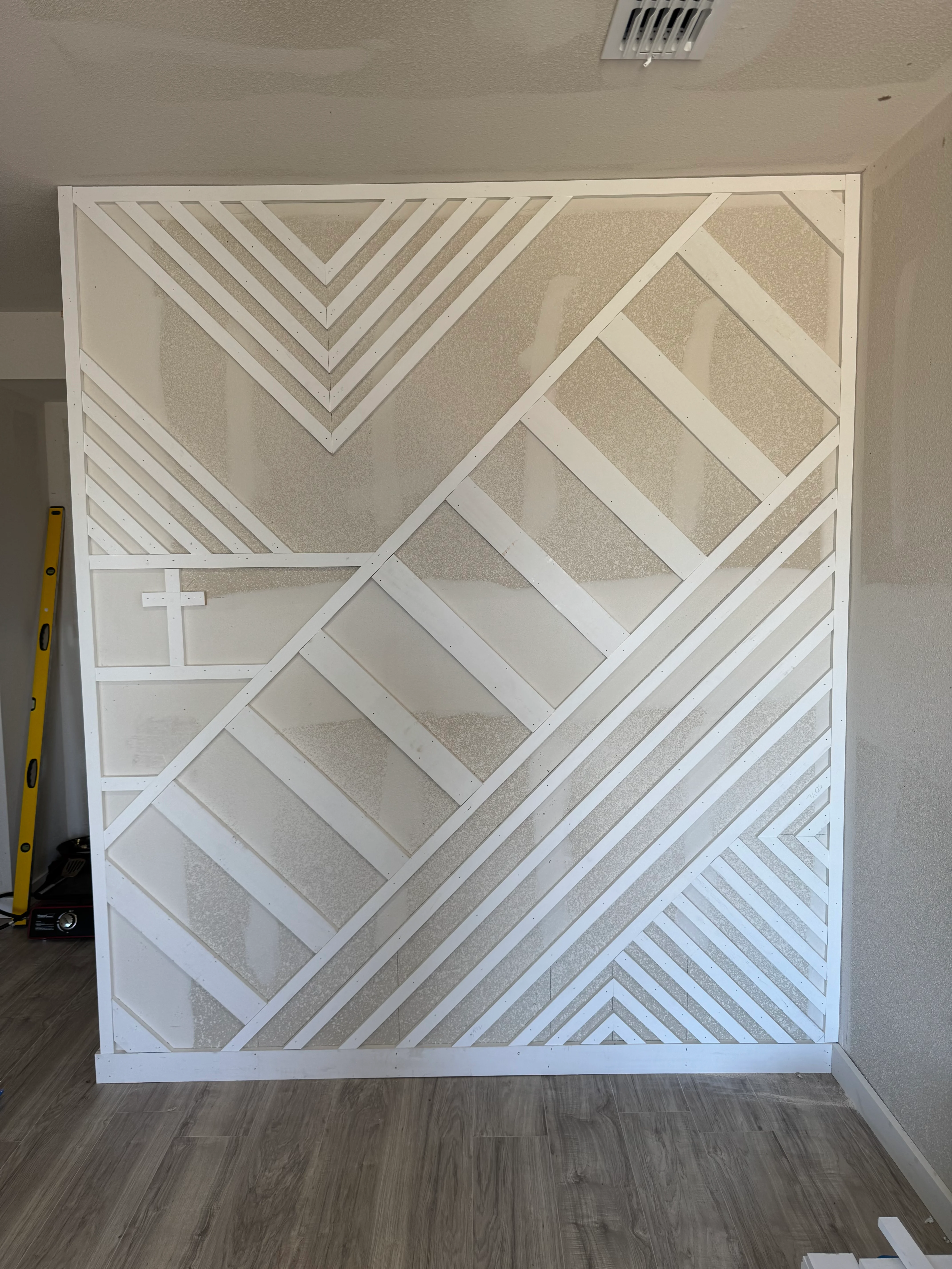 White geometric accent wall with diagonal stripes and framed patterns in neutral tones