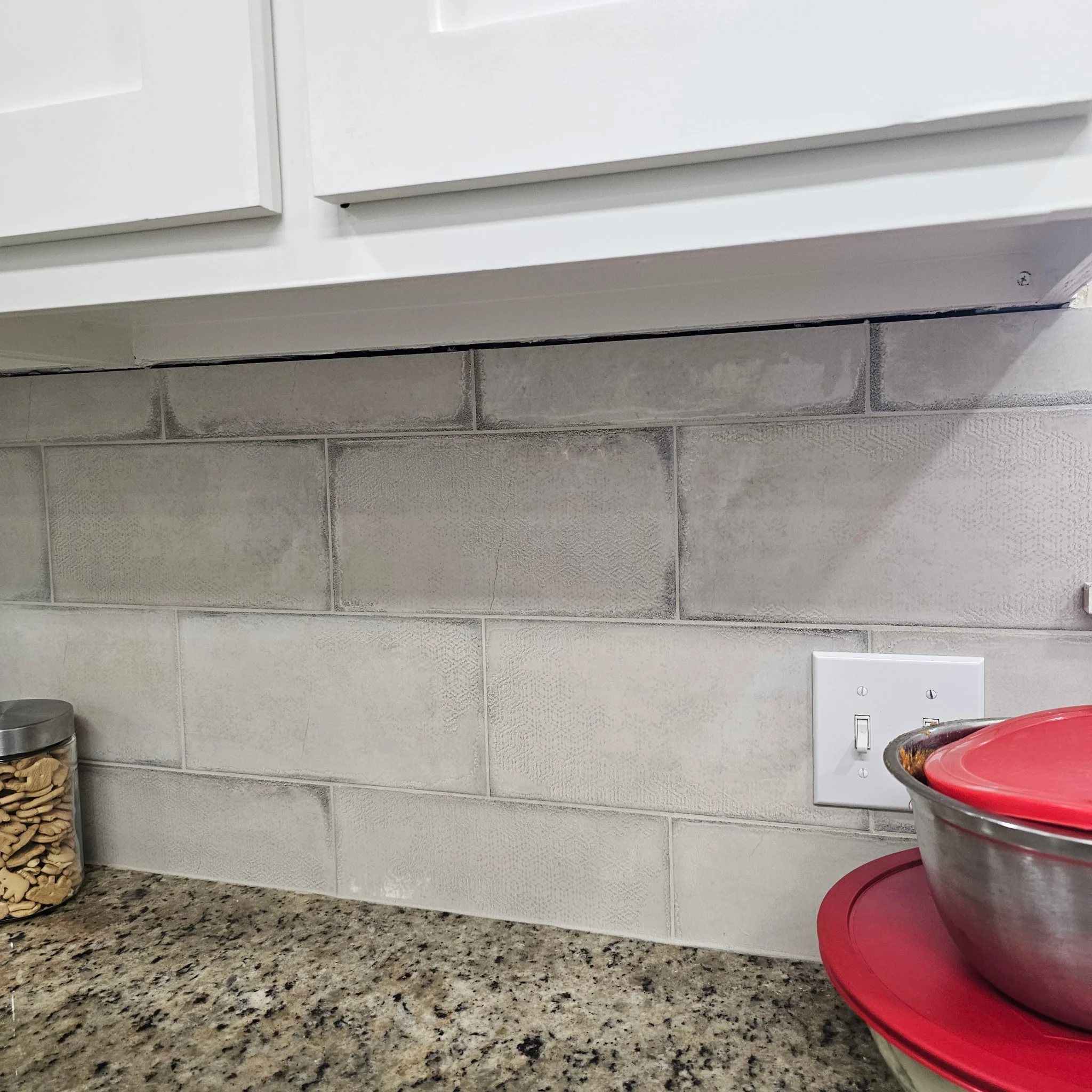 Light gray subway tile backsplash with textured finish installed above speckled granite countertop