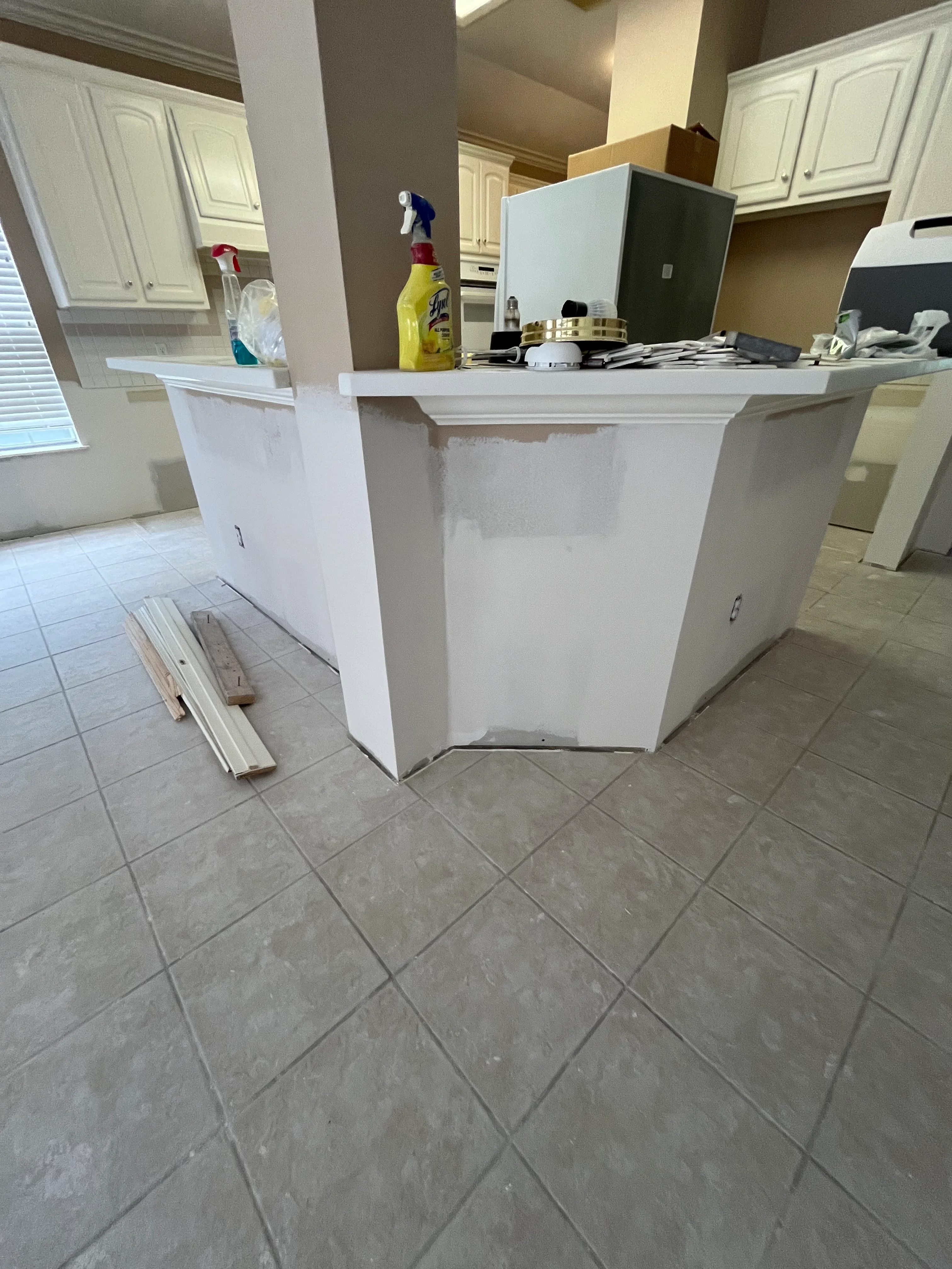 White drywall kitchen island under construction with finished cabinetry visible in background