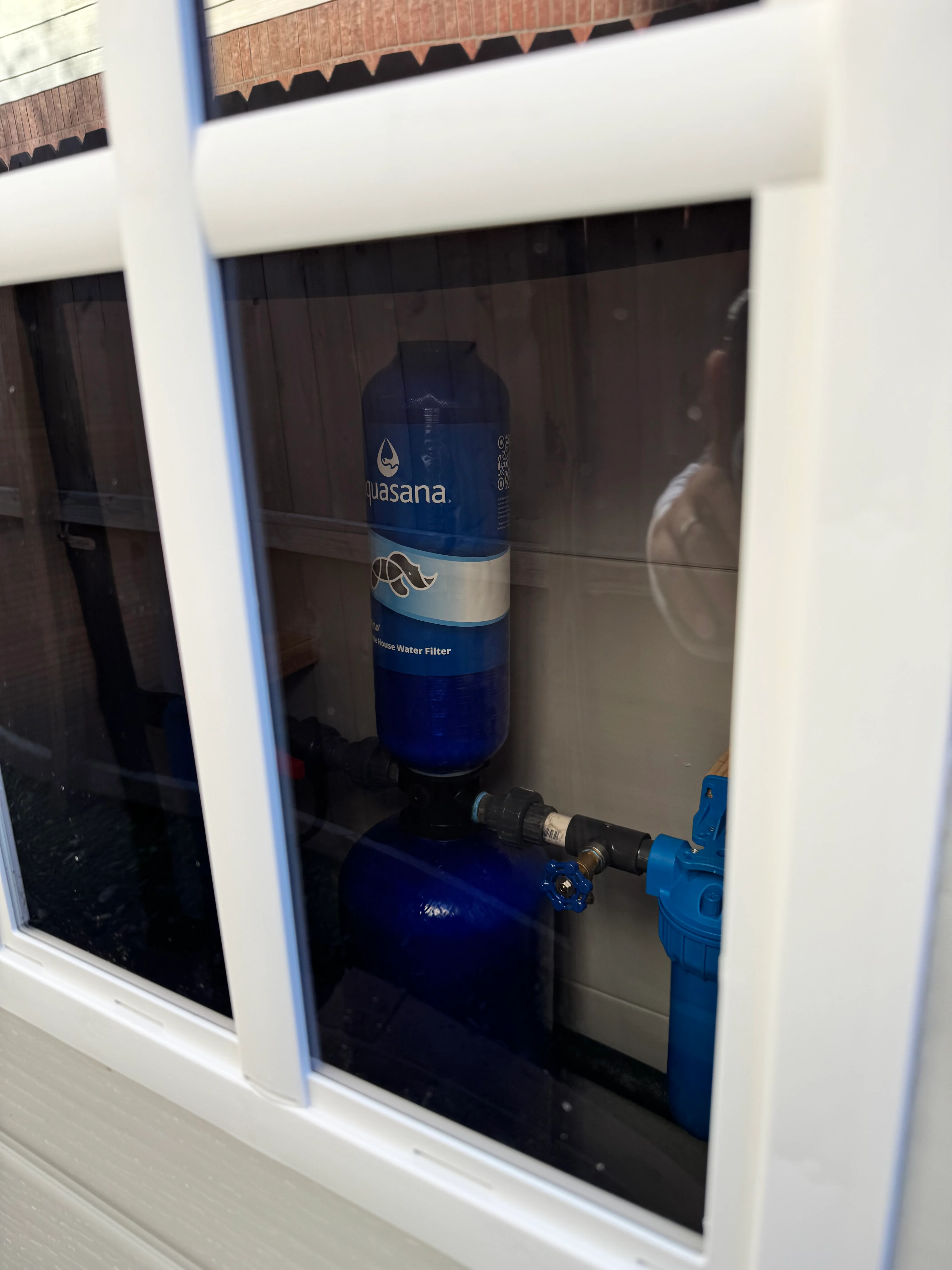 Aquasana water filter system installed in white cabinet with glass doors