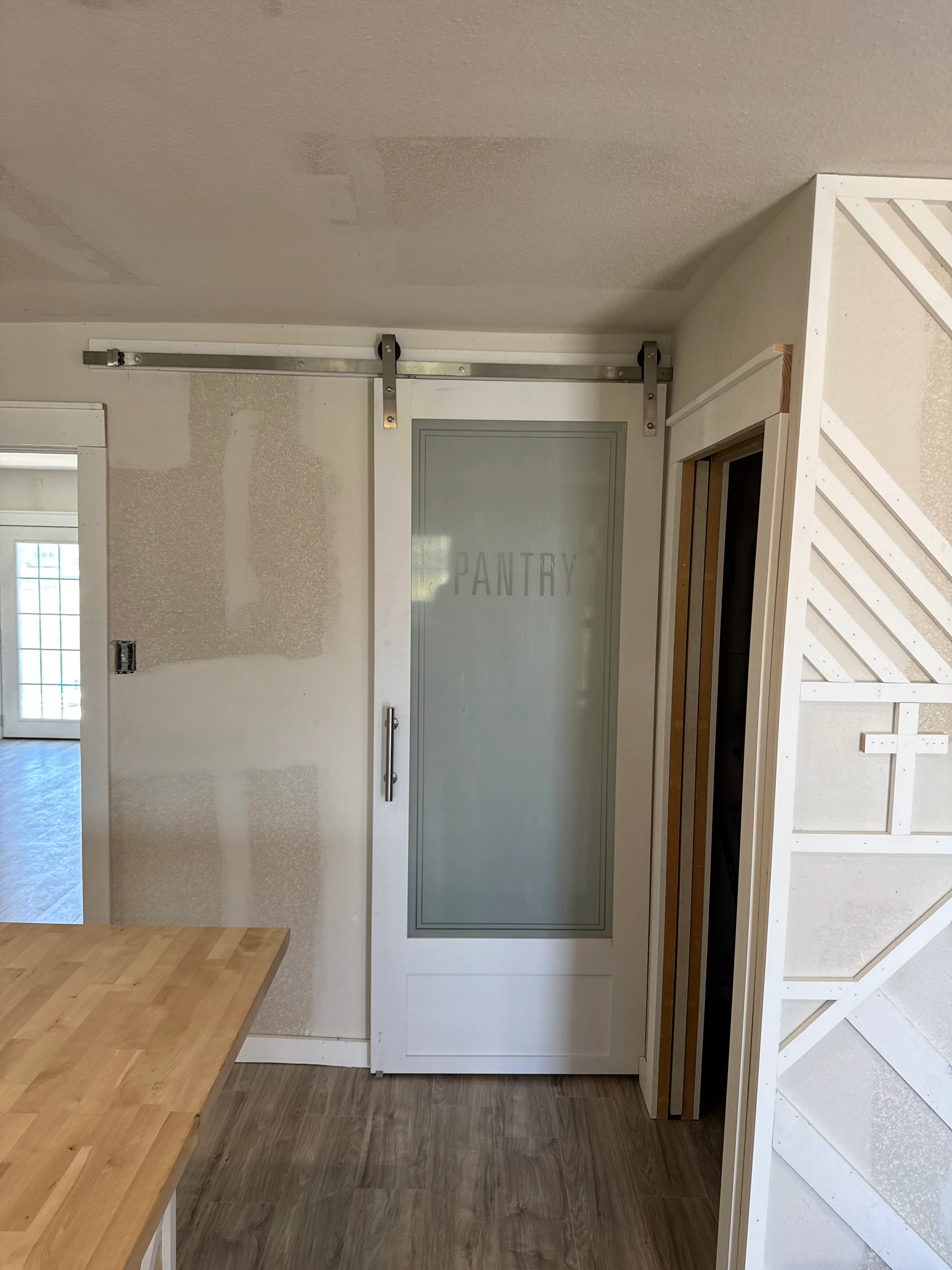 White barn door pantry with frosted glass panel and metal sliding track hardware in modern kitchen