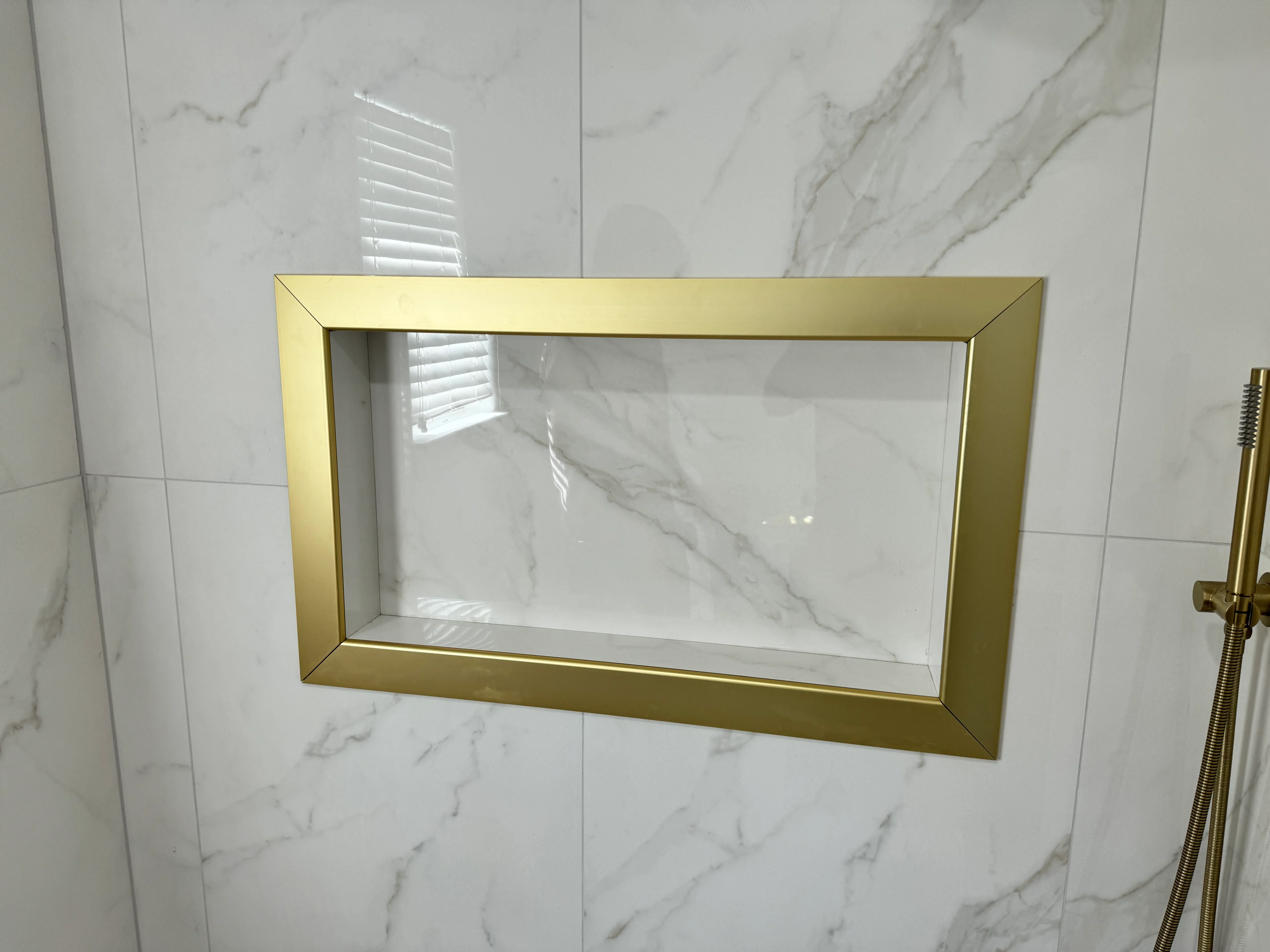 Marble bathroom wall with gold-framed recessed niche shelf and brass plumbing fixtures