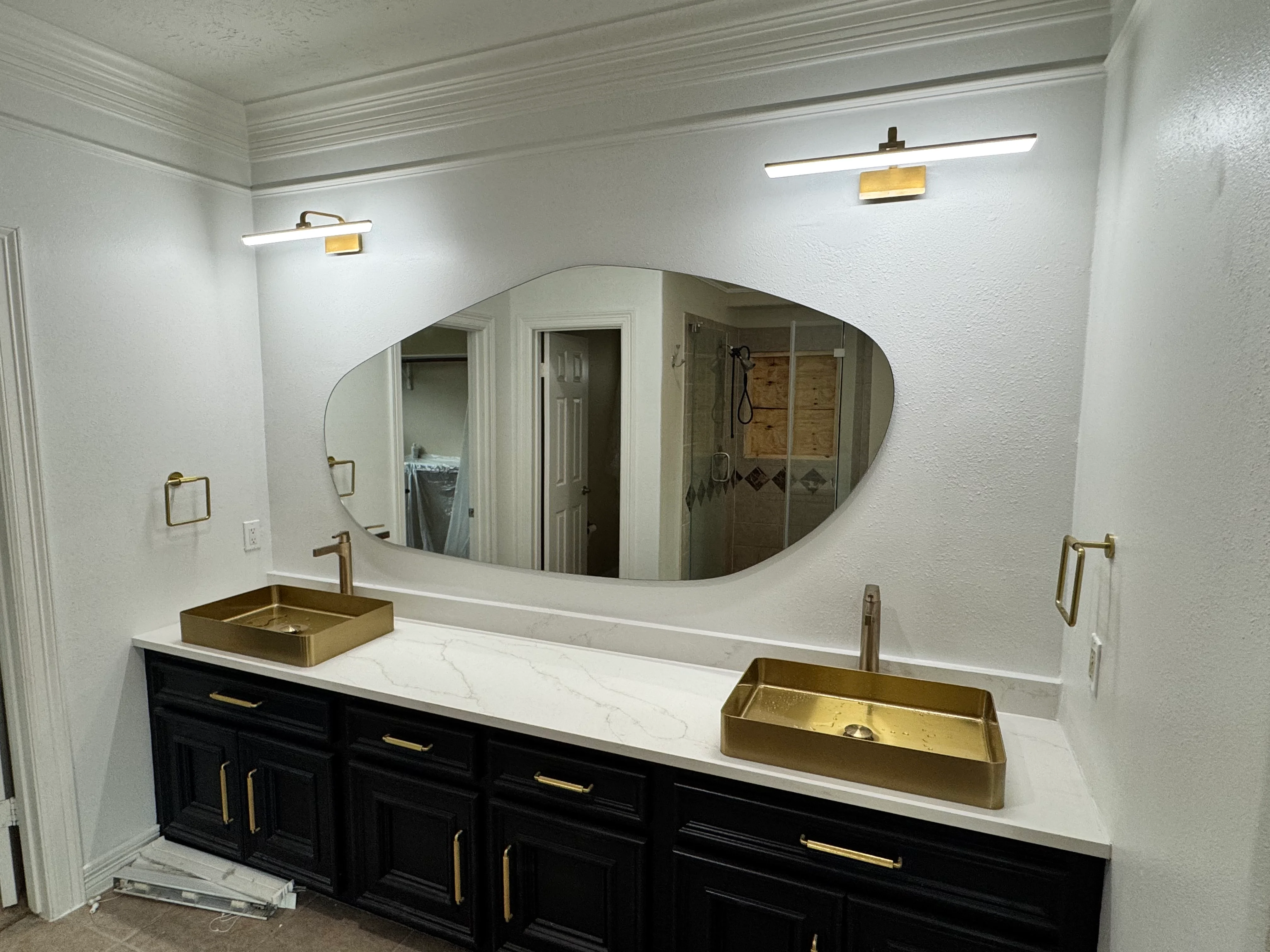 Modern bathroom vanity with black cabinets, white marble countertop, dual brass sinks, and large oval mirror