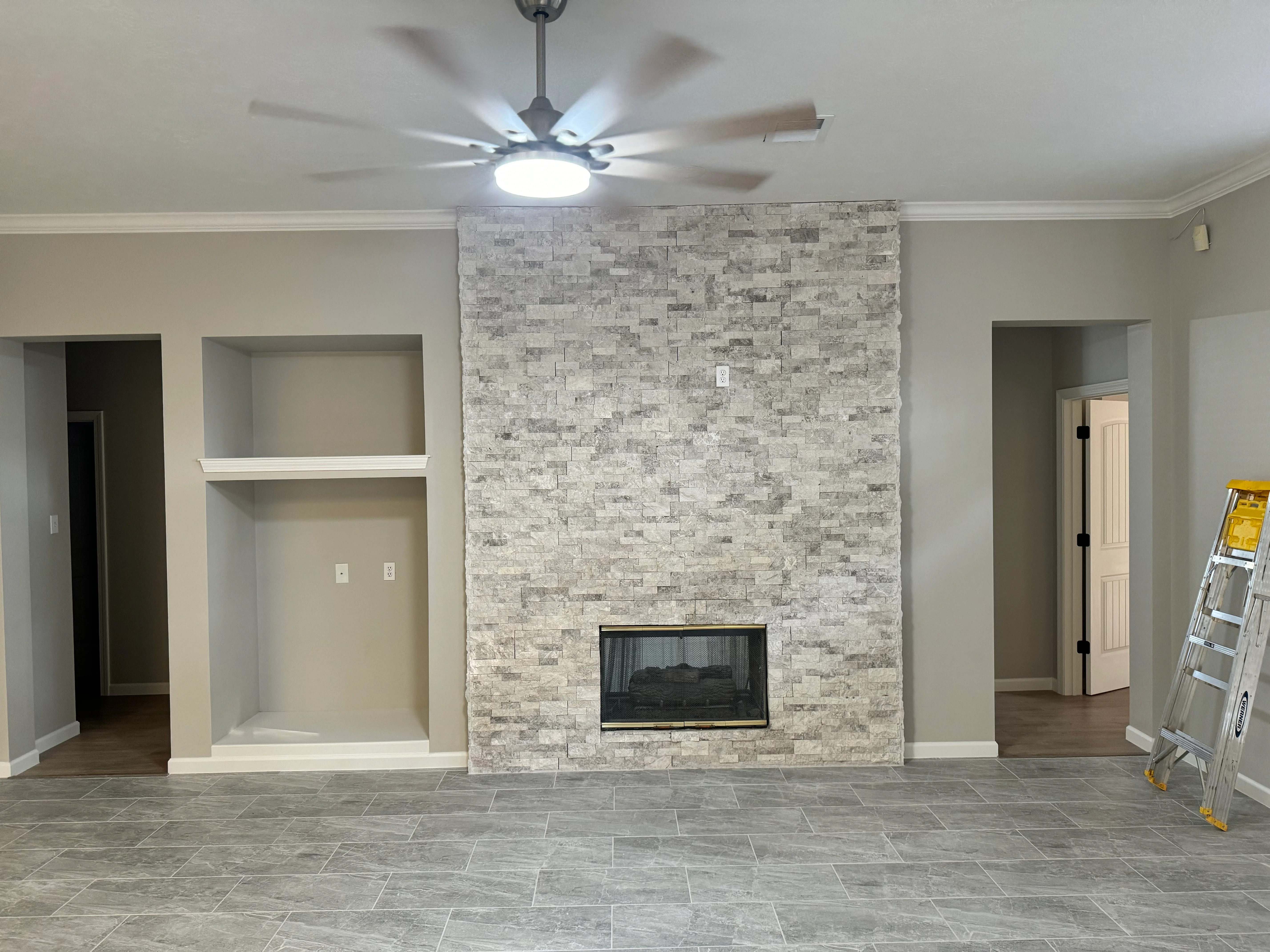 Modern living room with stacked stone fireplace wall, built-in shelving, and tile flooring