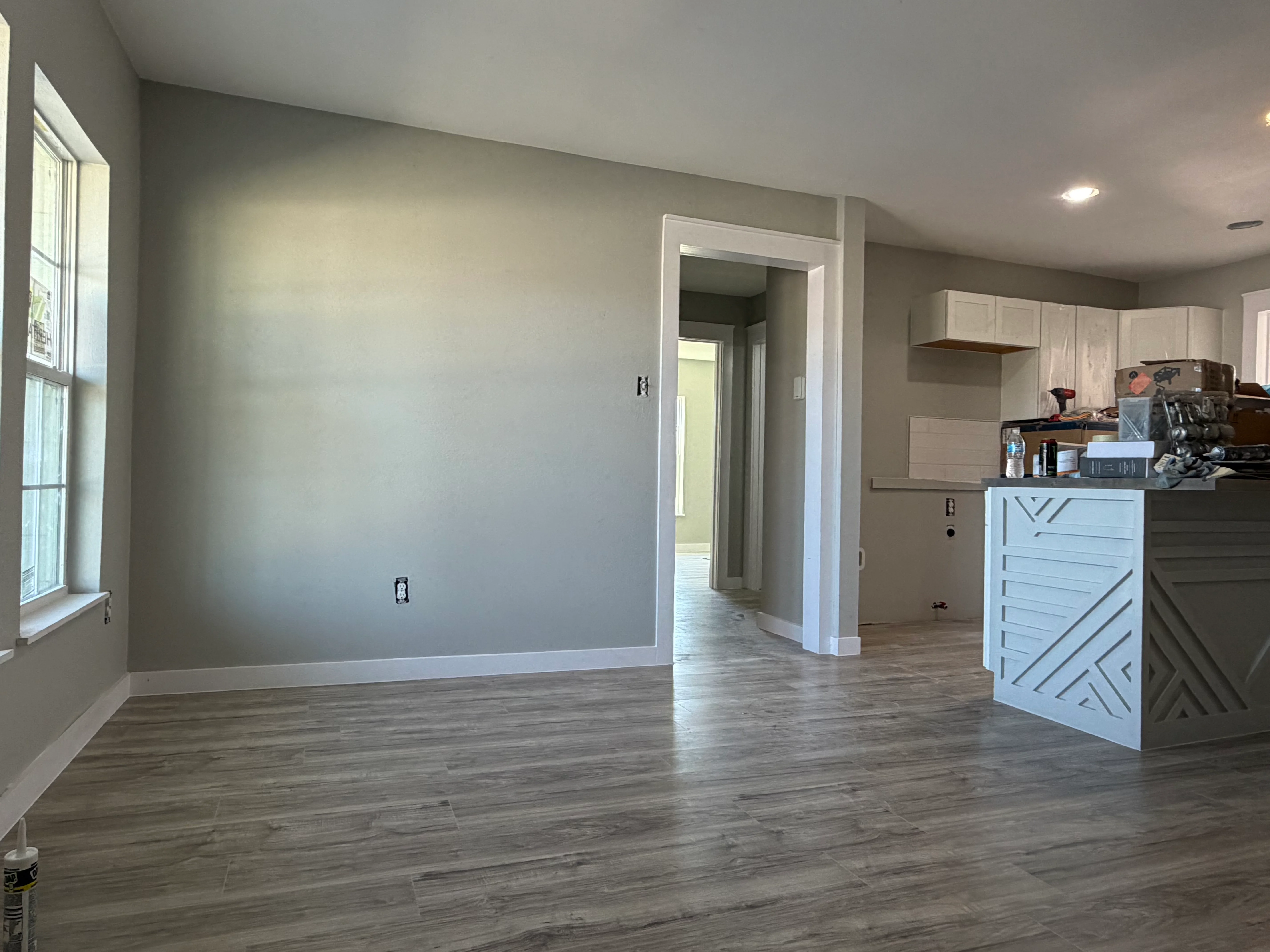 Open concept kitchen and living room with new flooring, drywall, and white cabinetry