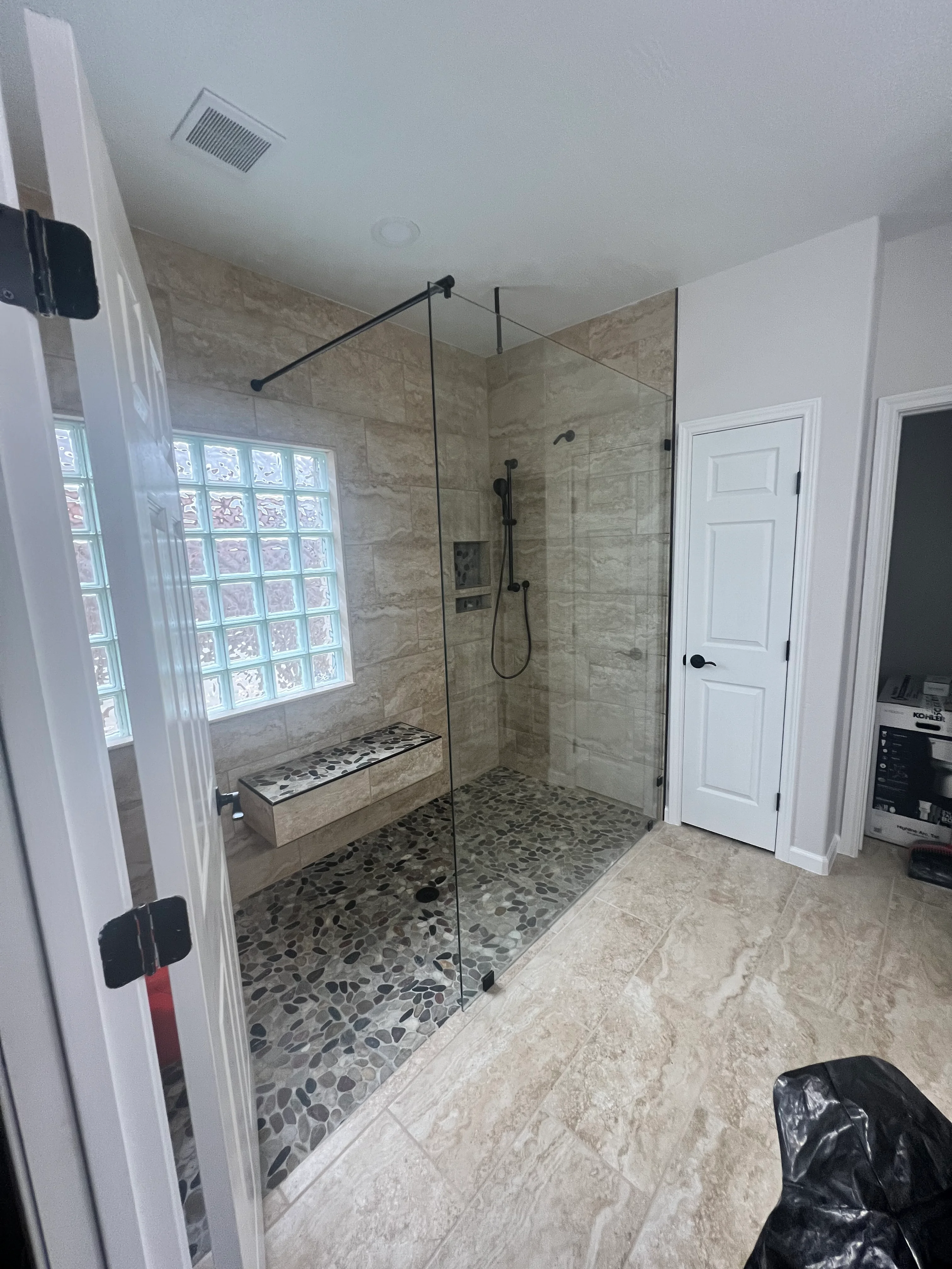 Modern frameless glass shower enclosure with travertine tile walls and pebble mosaic floor