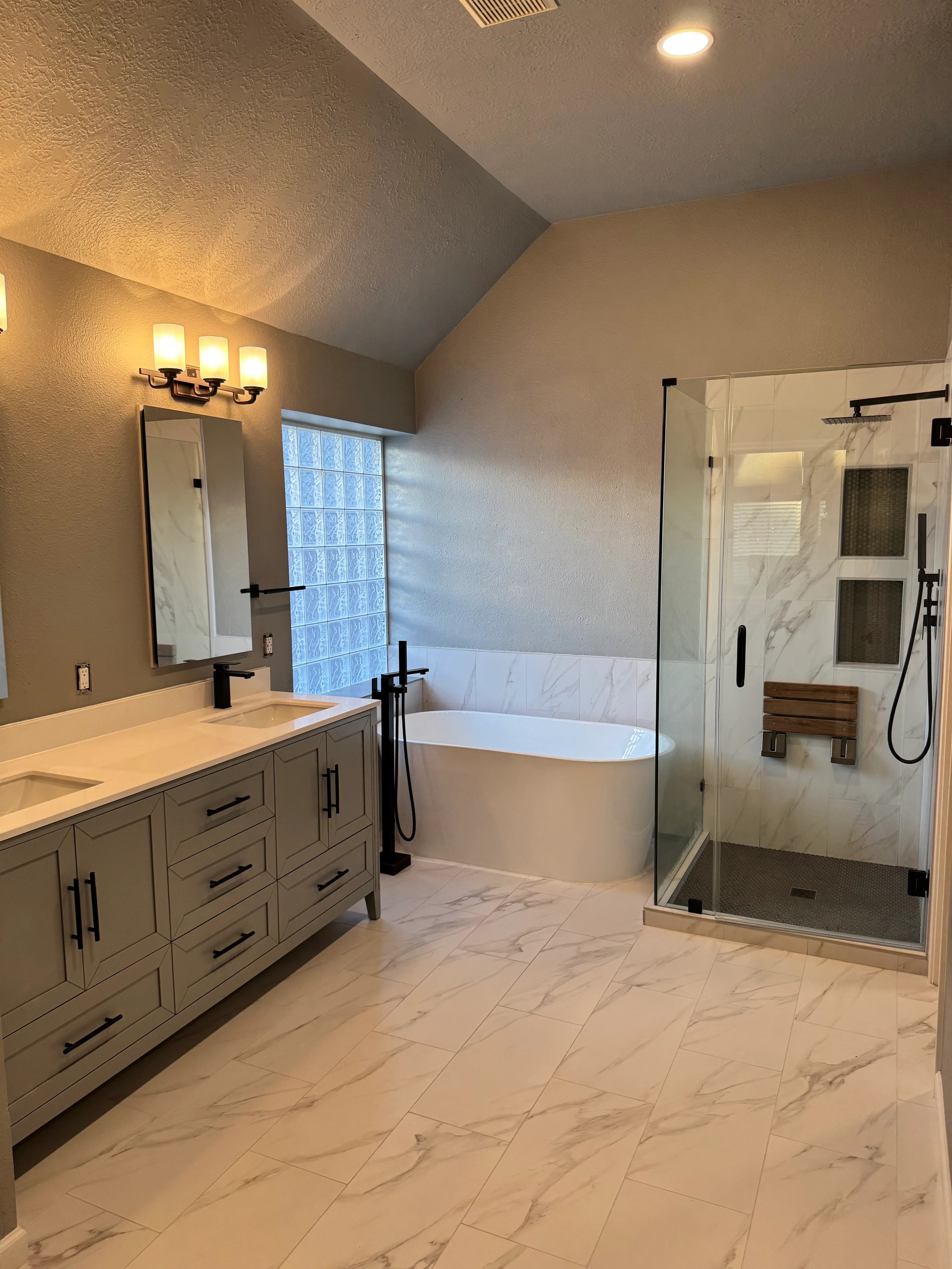 Modern master bathroom with white freestanding tub, glass shower enclosure, and gray cabinetry vanity