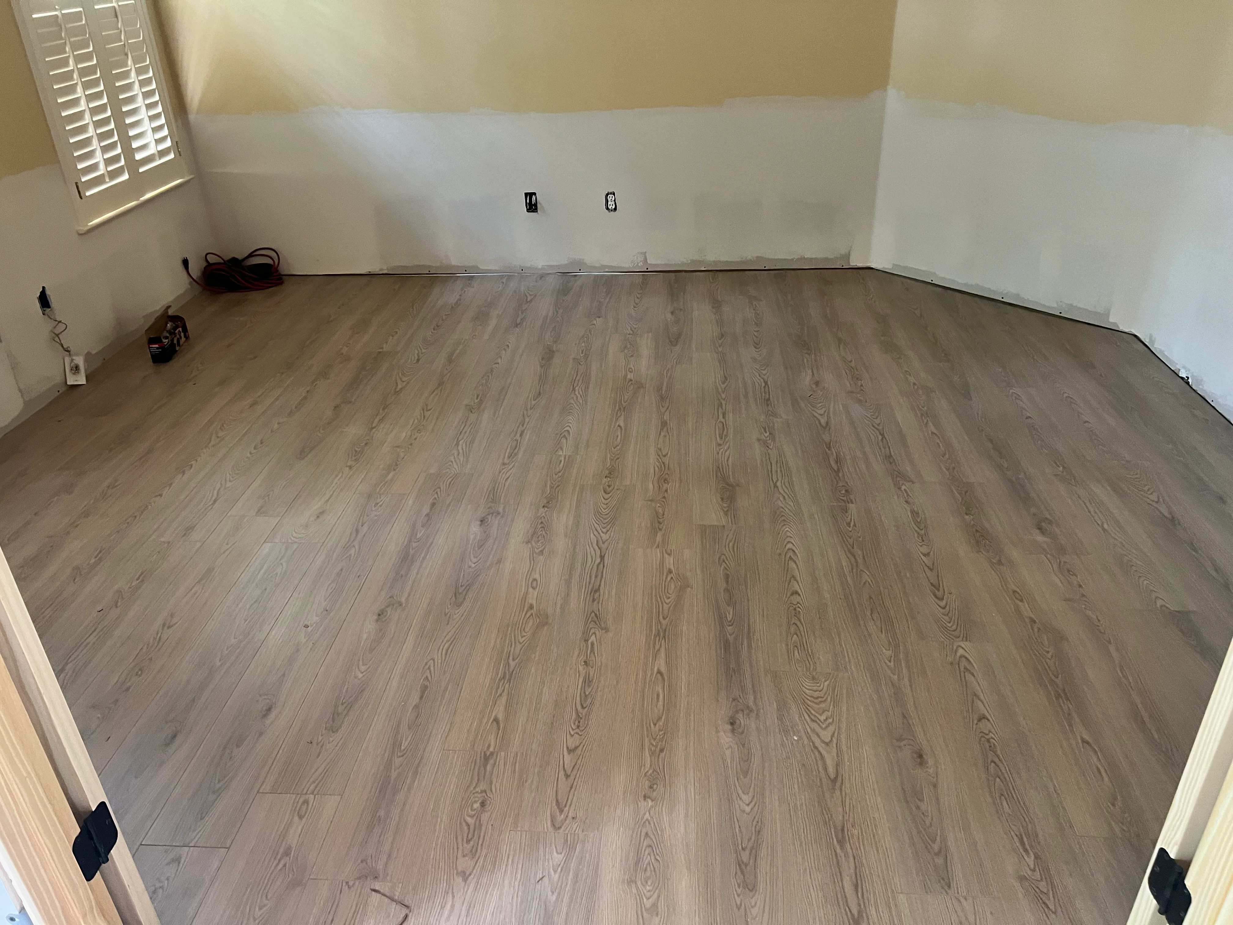 Gray wood-grain luxury vinyl plank flooring installed in residential room with fresh drywall