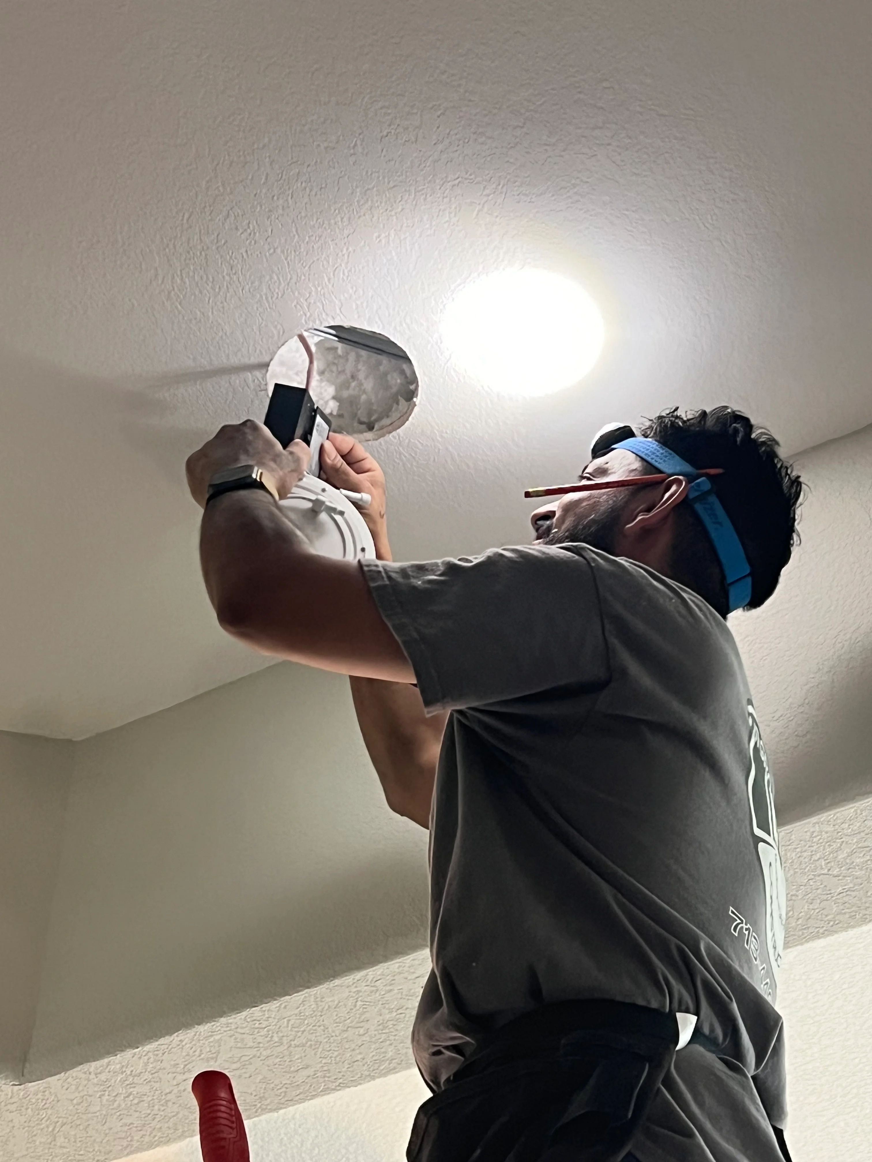 Electrician installing recessed ceiling light fixture in textured drywall ceiling
