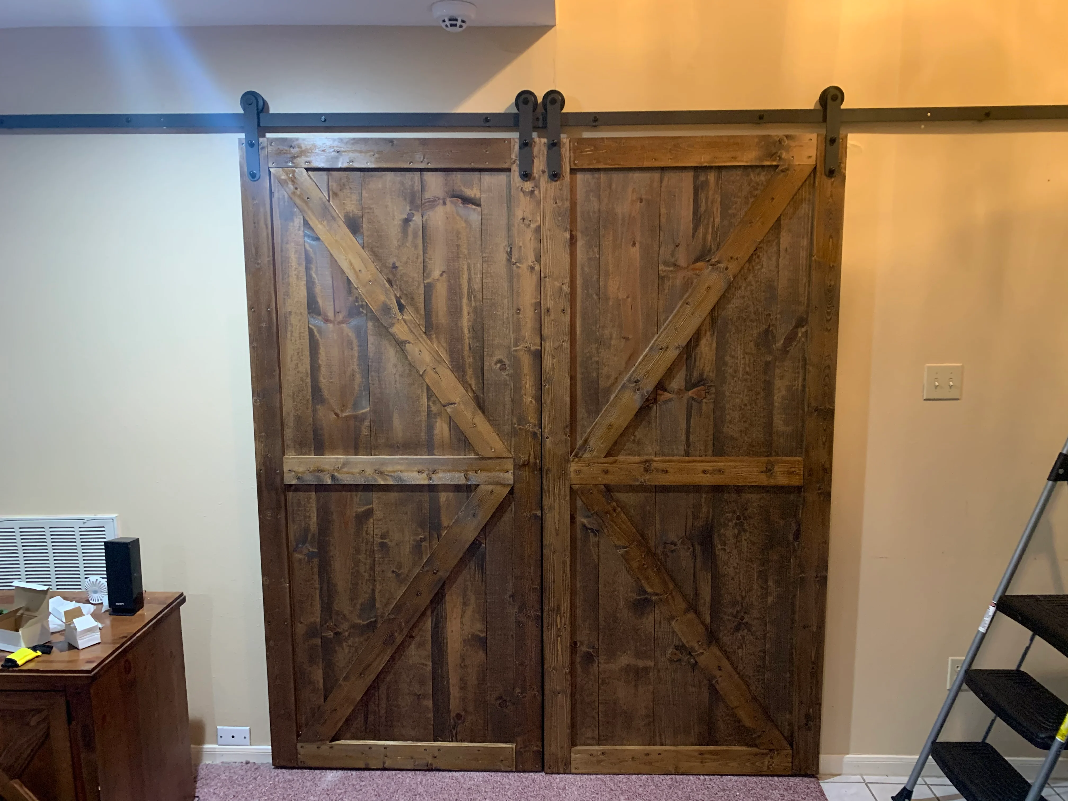 Two rustic wooden barn doors with X-braces on black sliding track hardware in modern interior