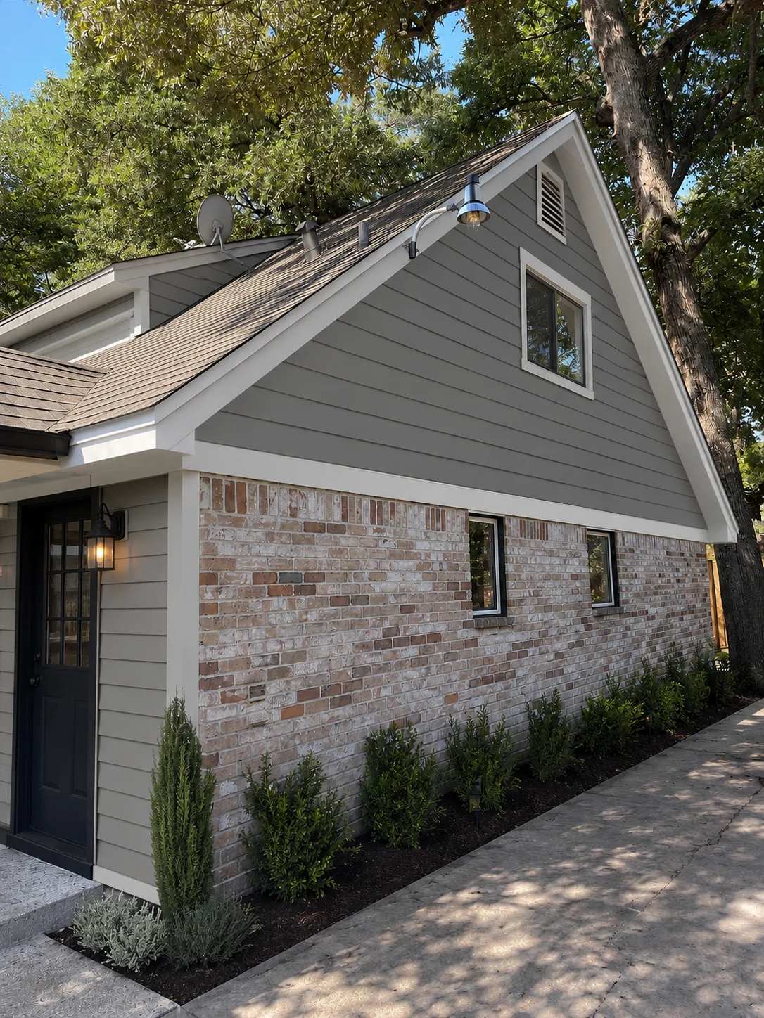 Modern home exterior with gray siding, brick base, and updated windows under mature trees
