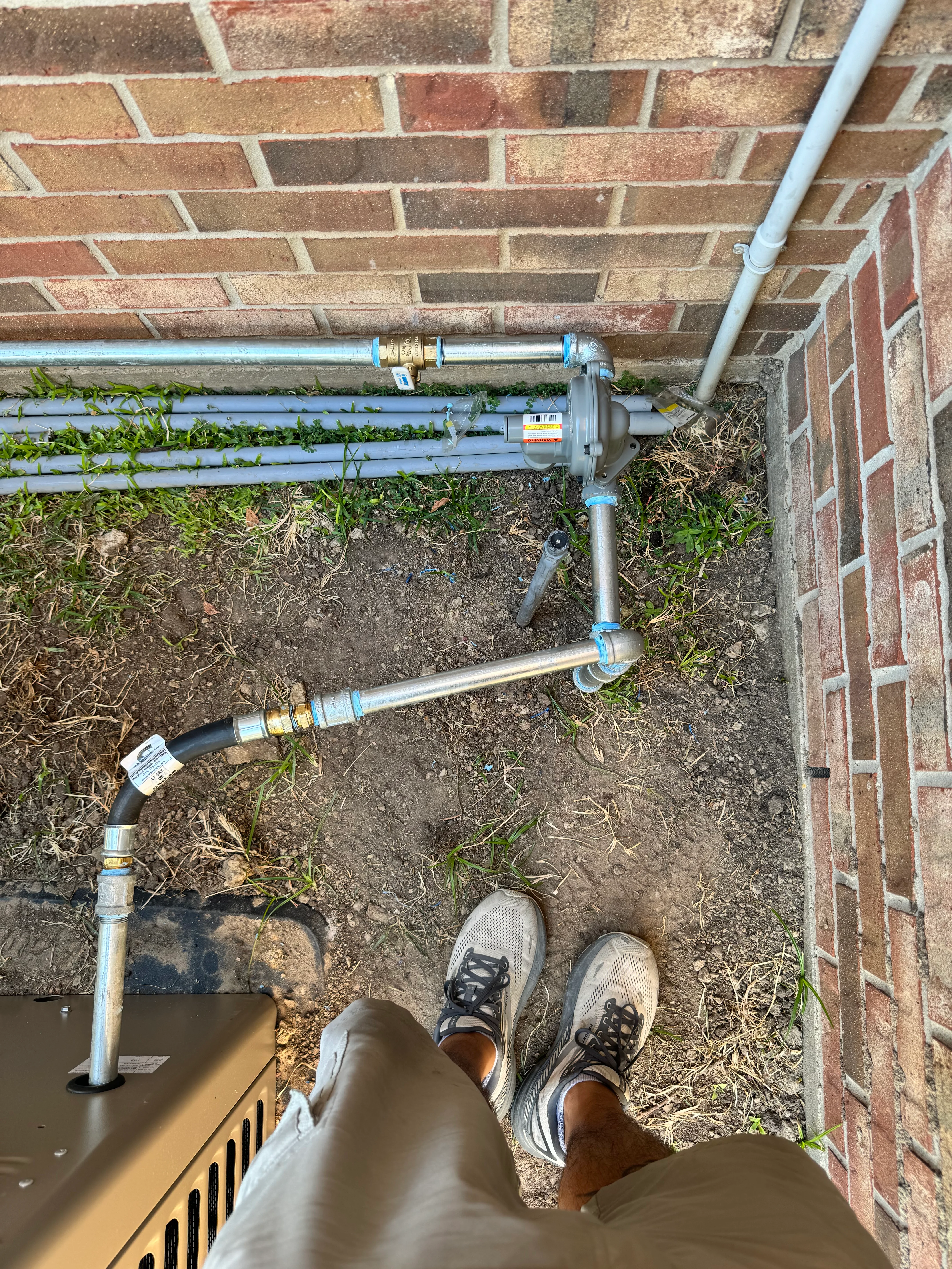 Blue PVC plumbing pipes with brass fittings installed at brick foundation base