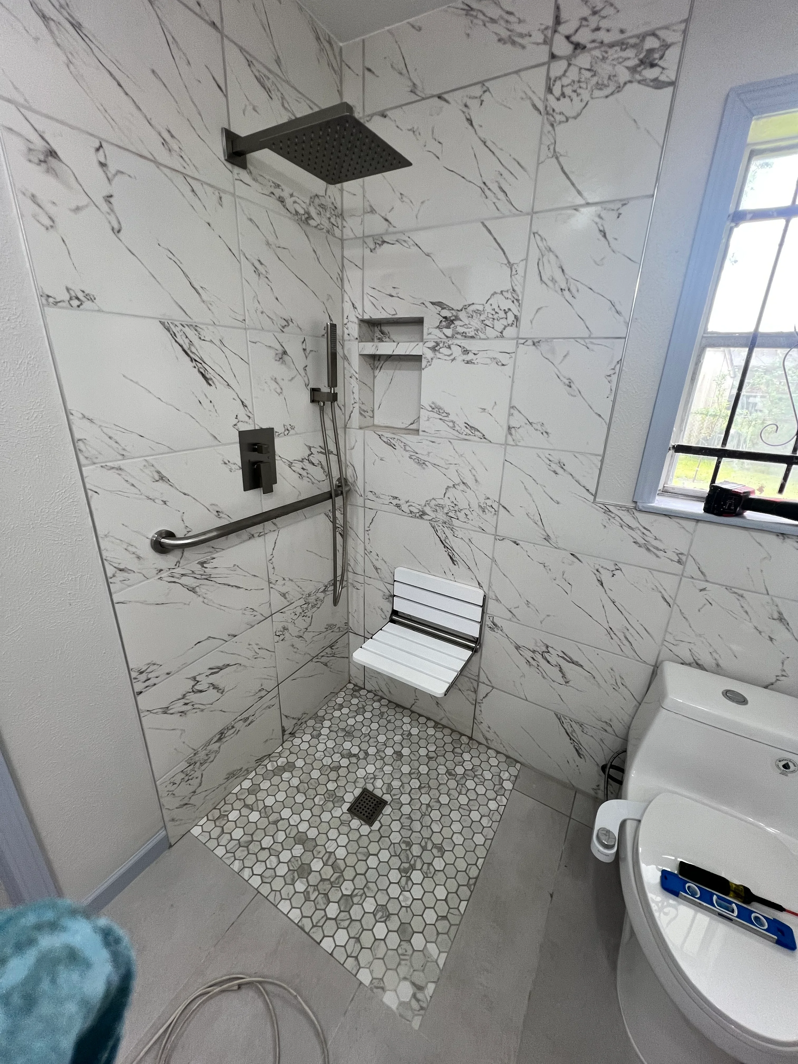 Modern shower with marble tile walls, rainfall showerhead, hexagonal floor tile, and built-in bench