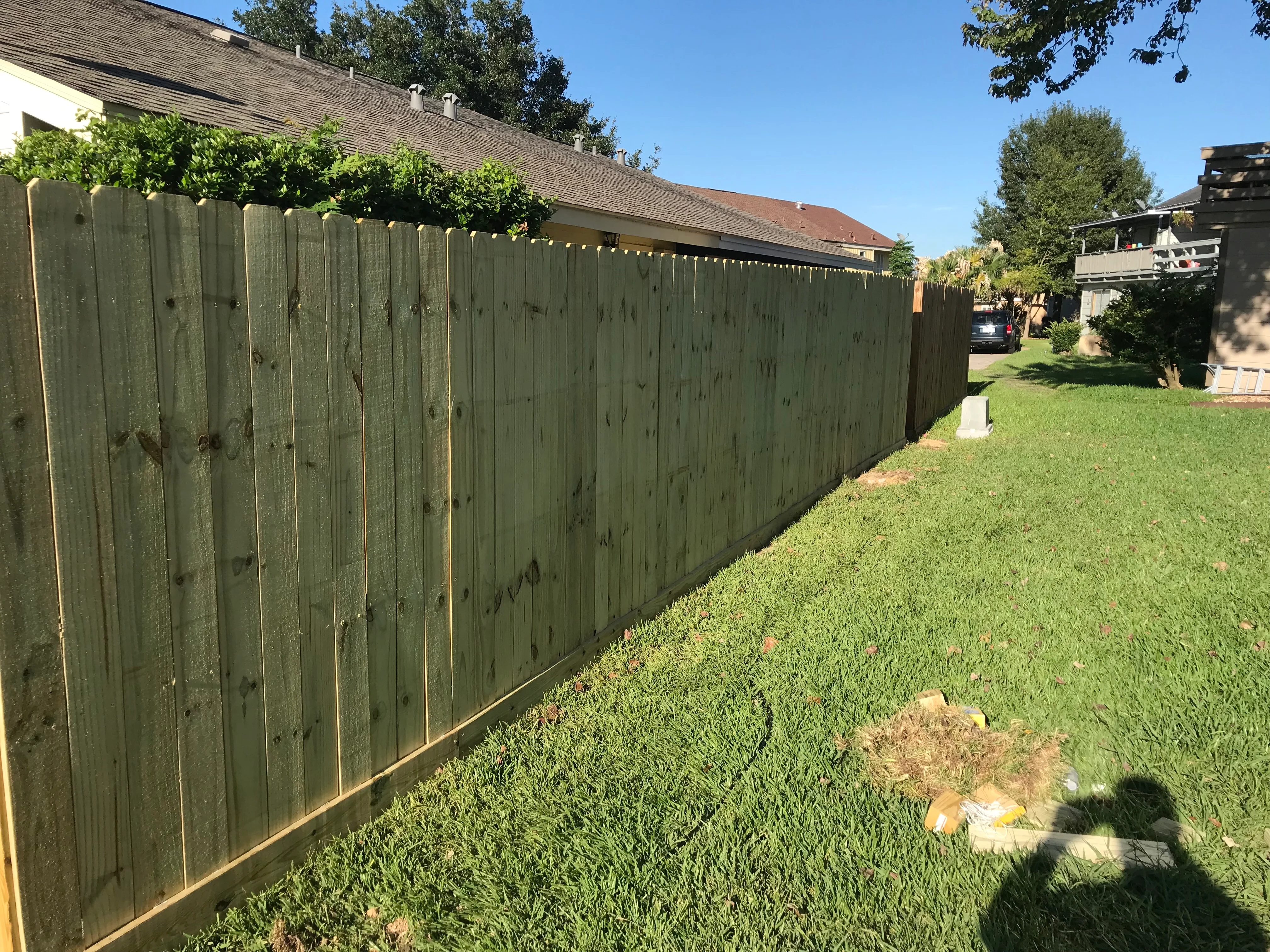 Green wood privacy fence installed along residential property line with brass hardware