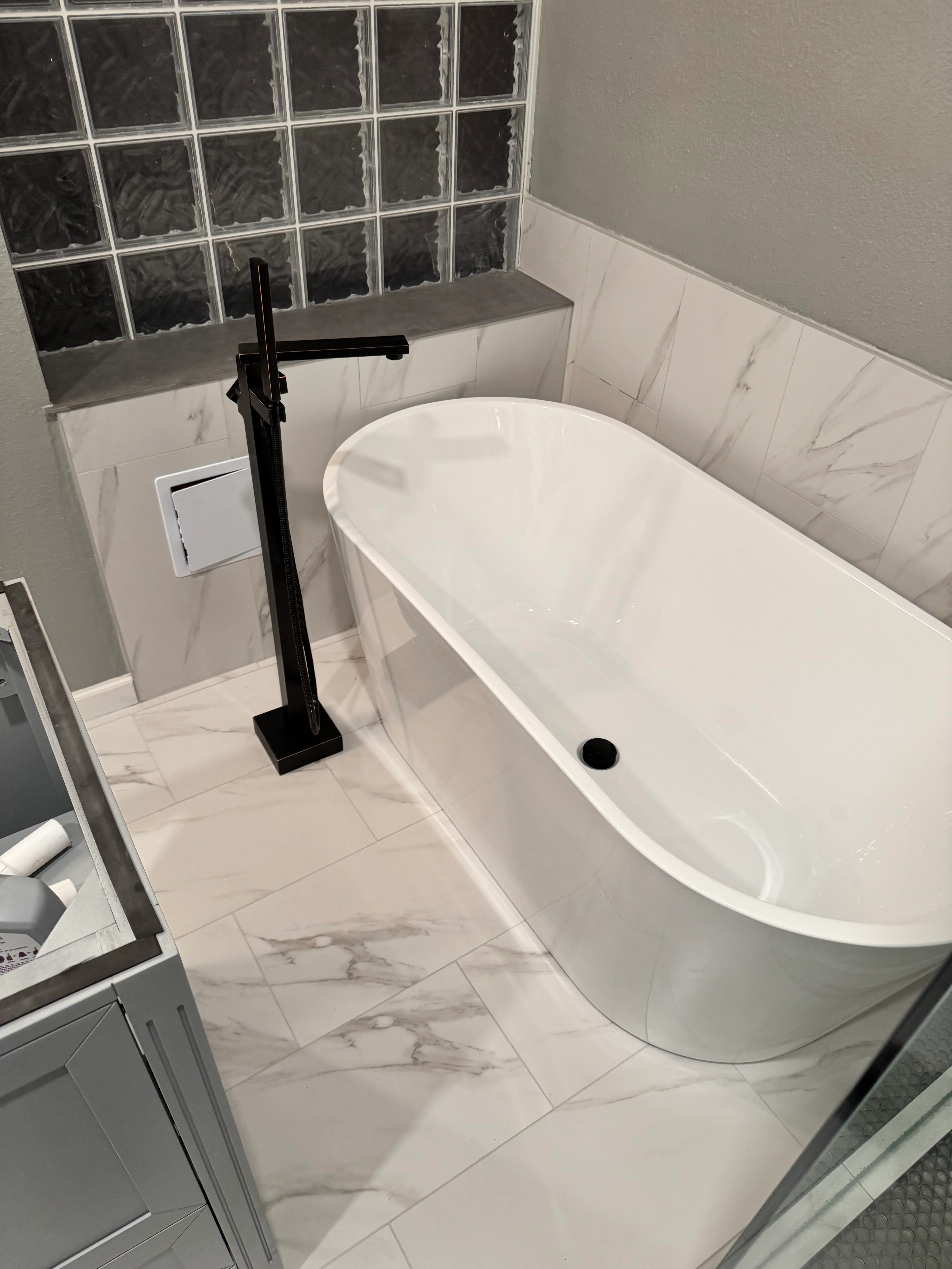 Modern bathroom with white freestanding tub, black faucet, and marble tile finishes