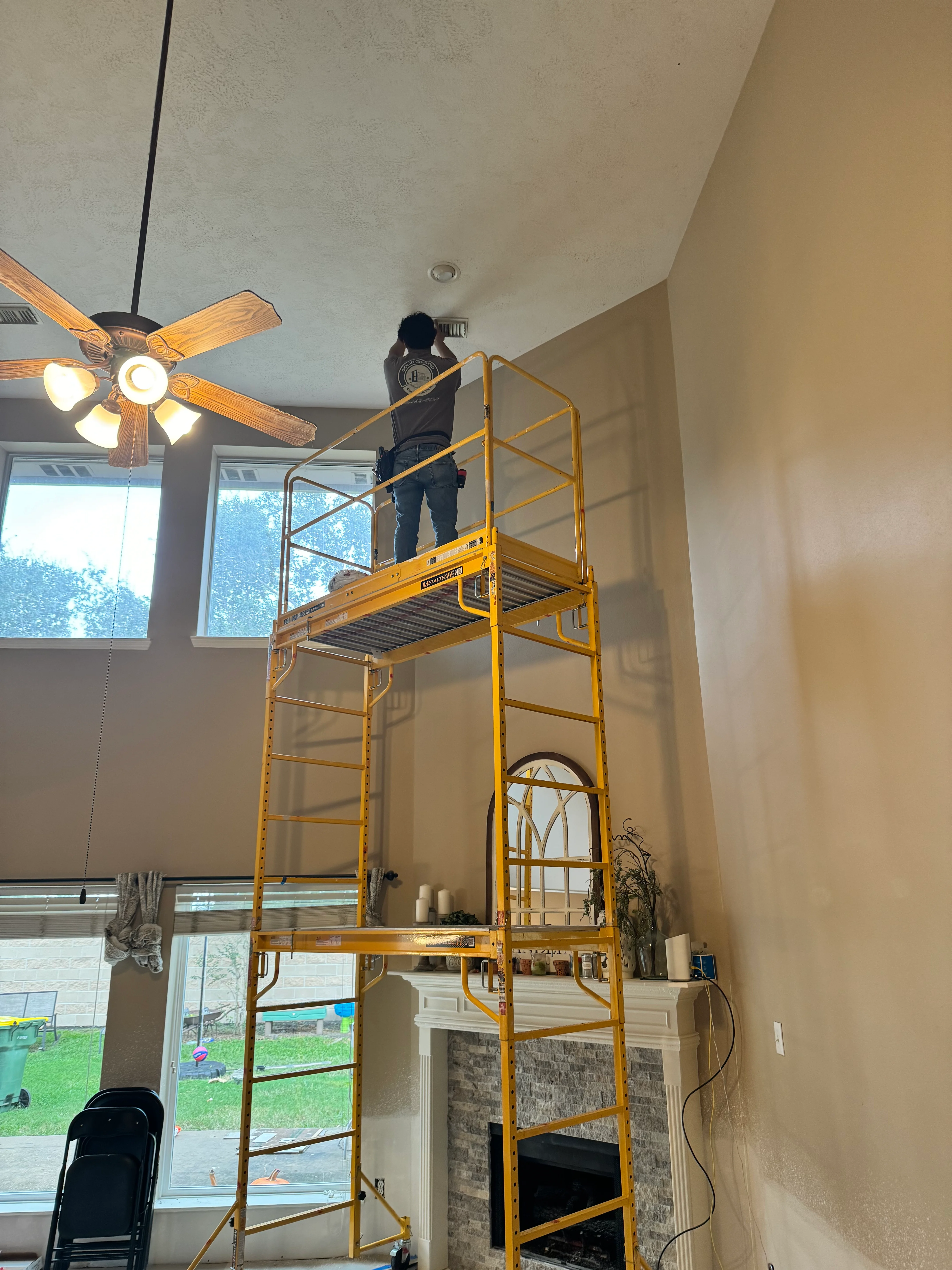 Electrician on scaffolding installing ceiling fan with lights in vaulted ceiling room